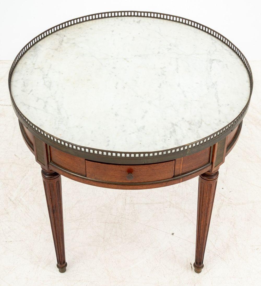 Louis XVI Style Walnut Circular Marble Top Lamp Table, with pierced brass galleried top on white Carrara marble, with two small drawers on four fluted tapered legs with brass tips. 22.5
