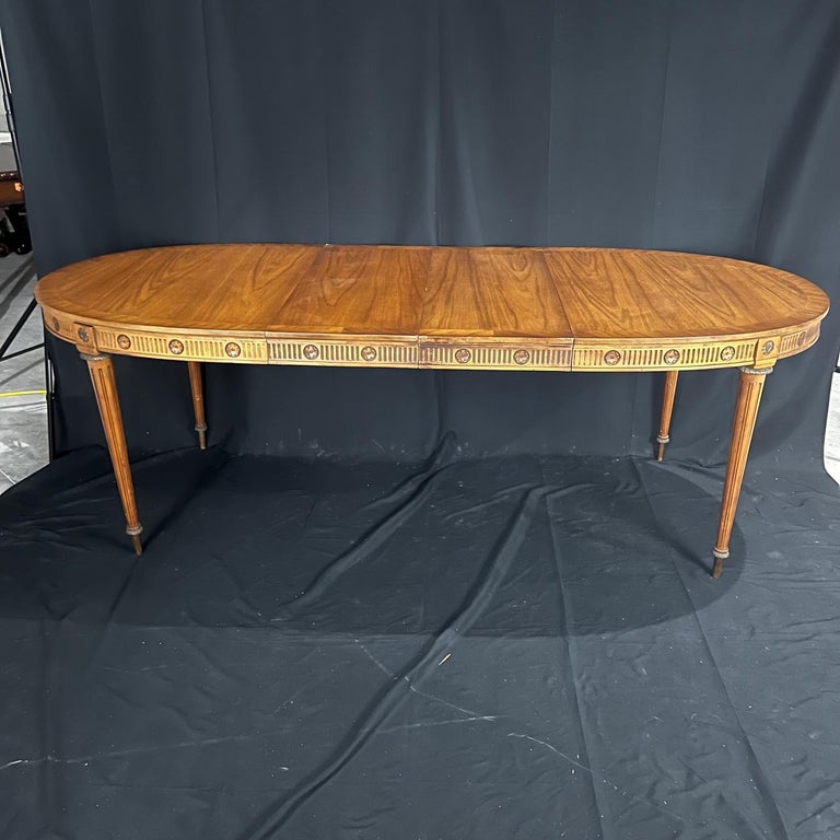 An outstanding and exceptional Louis XVI style dining table constructed from richly stained walnut having elegantly fluted and tapered legs with bronze adornments. Two leaves included. 
W 60.5 without leaves, 90” with leaves (each of the two leaves