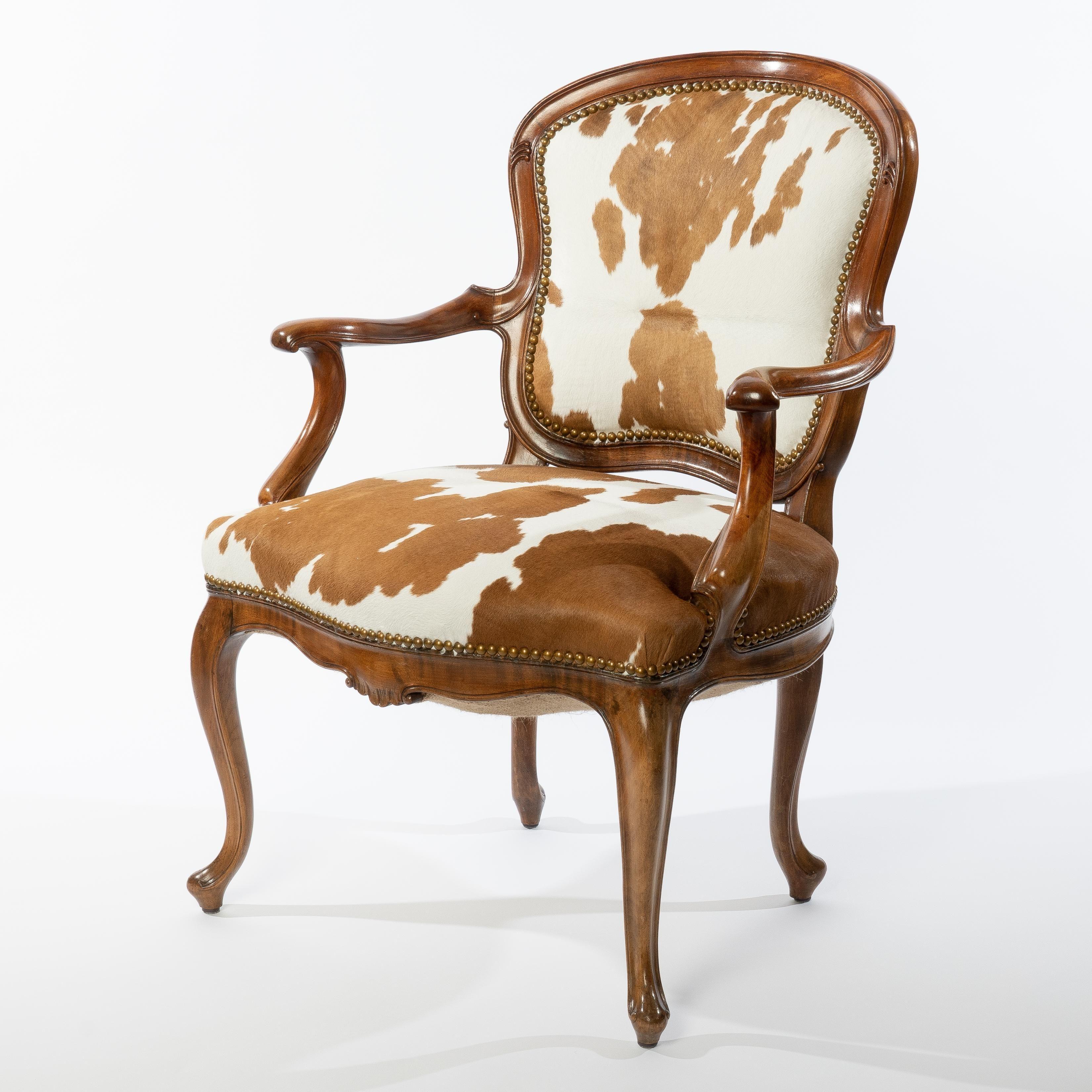 Superbly carved European walnut framed fauteuil in the Louis XVI taste. Back and seat have been re-webbed, filled, and upholstered in hair-on-hide calf skin with brass tacks. The exterior back is covered in a tan and white cotton gingham