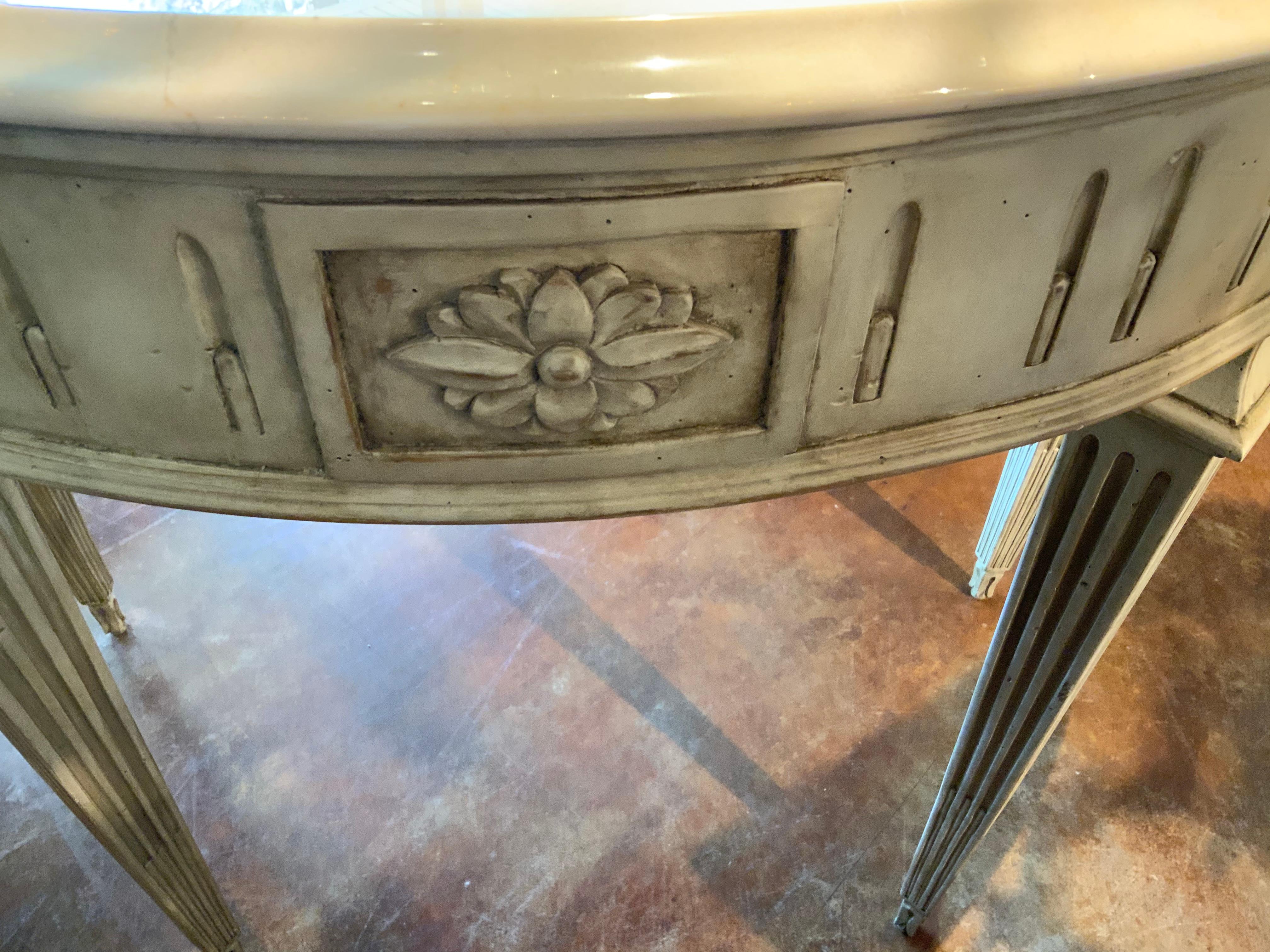 Stylized demi-lune shaped console, painted in a creamy white hue rising on Louis XVI-style
Reeded legs. A floral carved motif at the front center and sides.