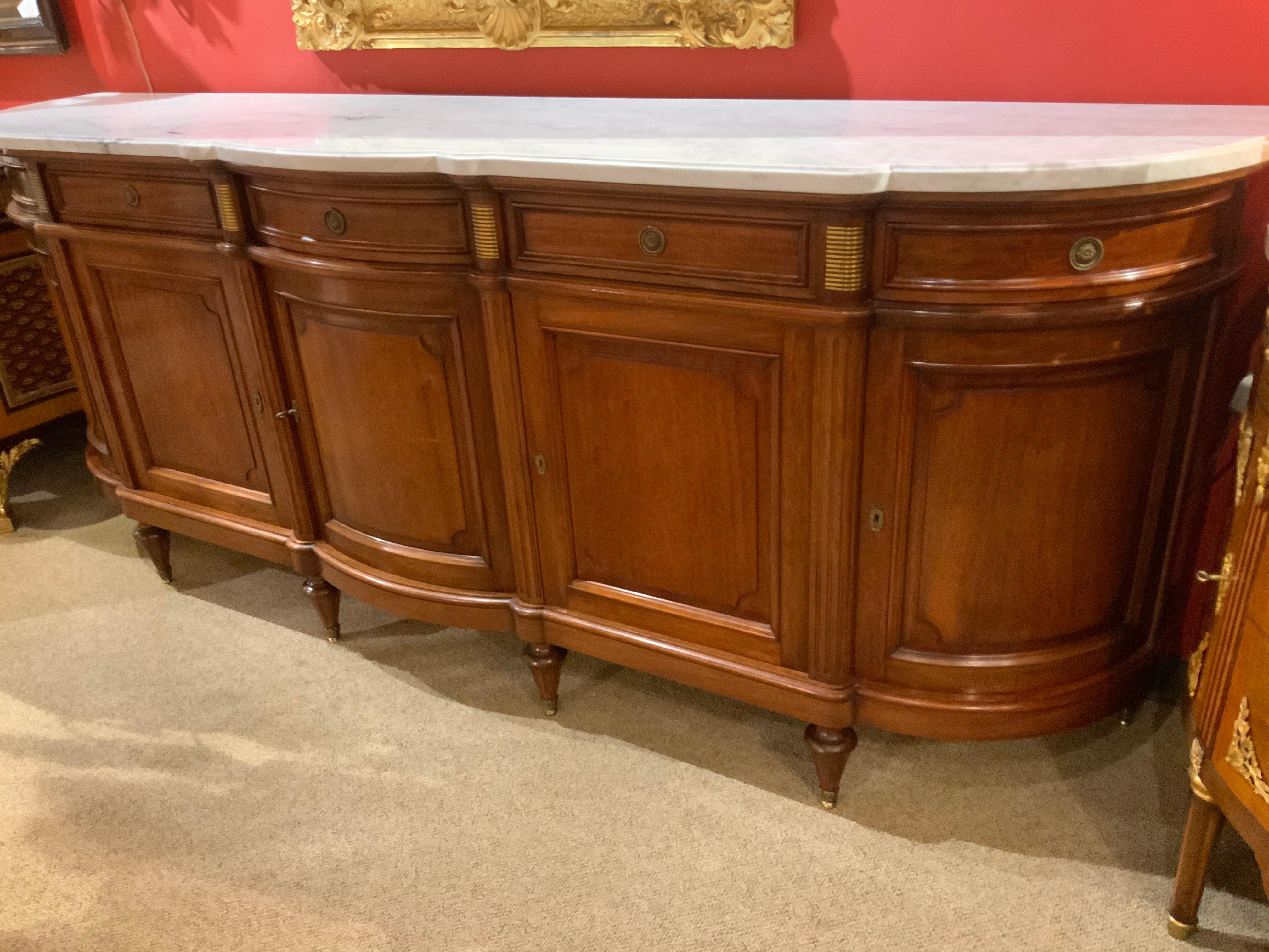 Excellent quality sideboard made of mahogany with a white marble top over a conforming case.
This piece has five doors with five drawers above. It rises on Louis XVI style leg with sabots.
The piece is beautifully curved in the center and on the