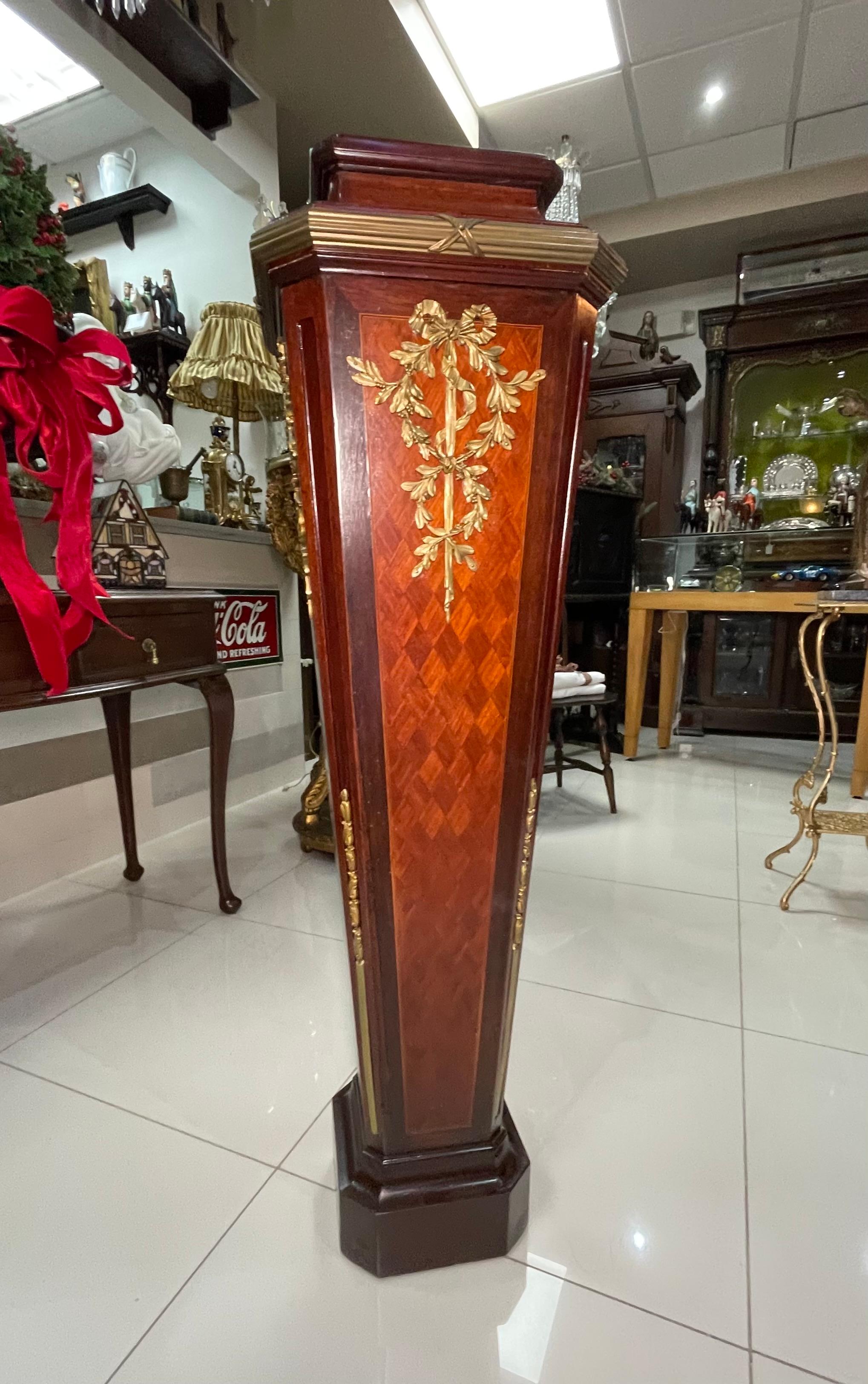 Si tratta di un piedistallo in legno in bronzo in stile Luigi XVI. Raffigura un alto piedistallo a quattro pareti affusolate, decorato con un parquet intarsiato con un motivo a rombi. Ogni parte superiore della parete è ornata da un lungo nastro di