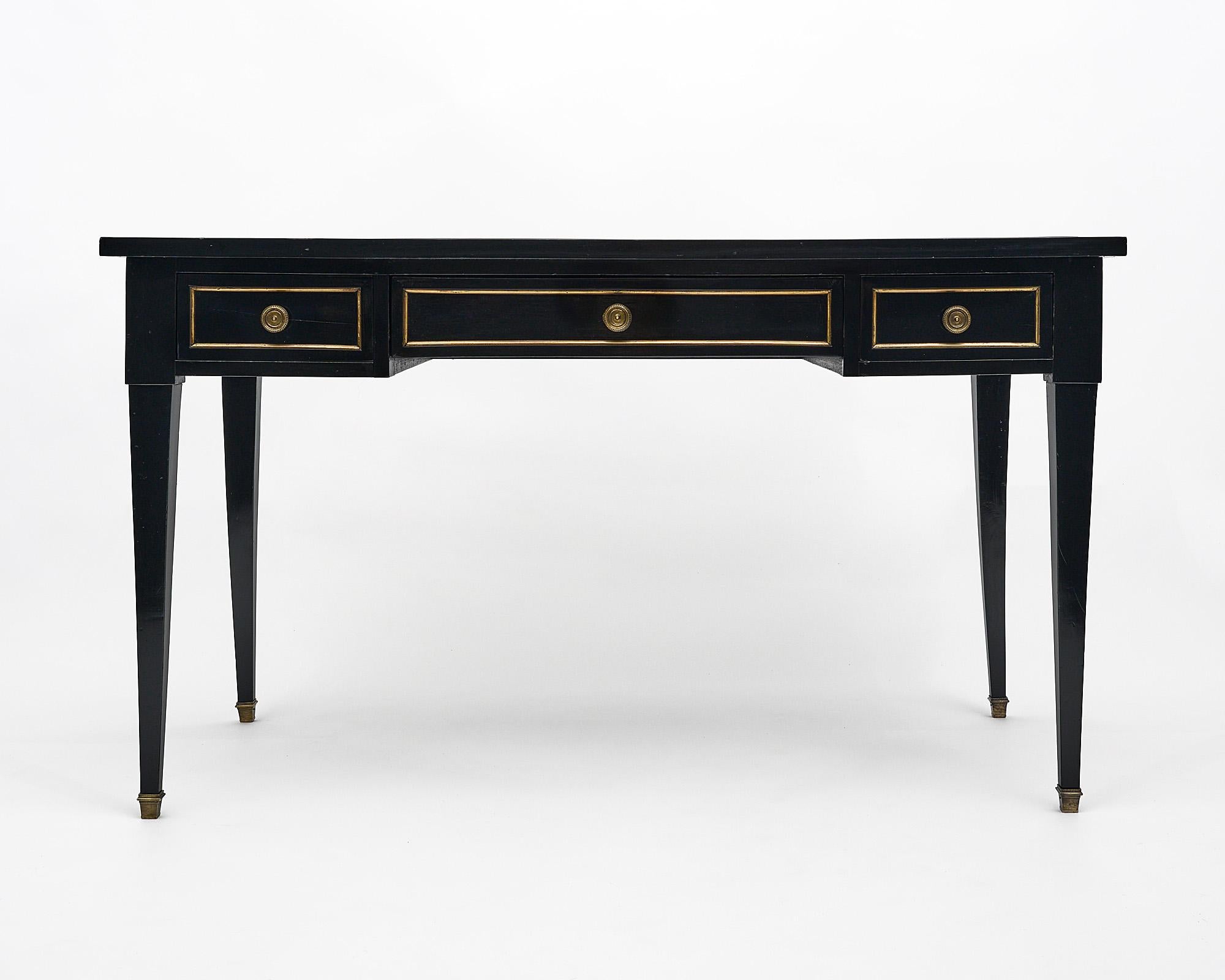 Desk, French, in the Louis XVI style made of mahogany that has been ebonized and finished in a museum quality French polish. This elegant writing desk features three dovetailed drawers, square tapered legs, and gilt brass throughout. This table