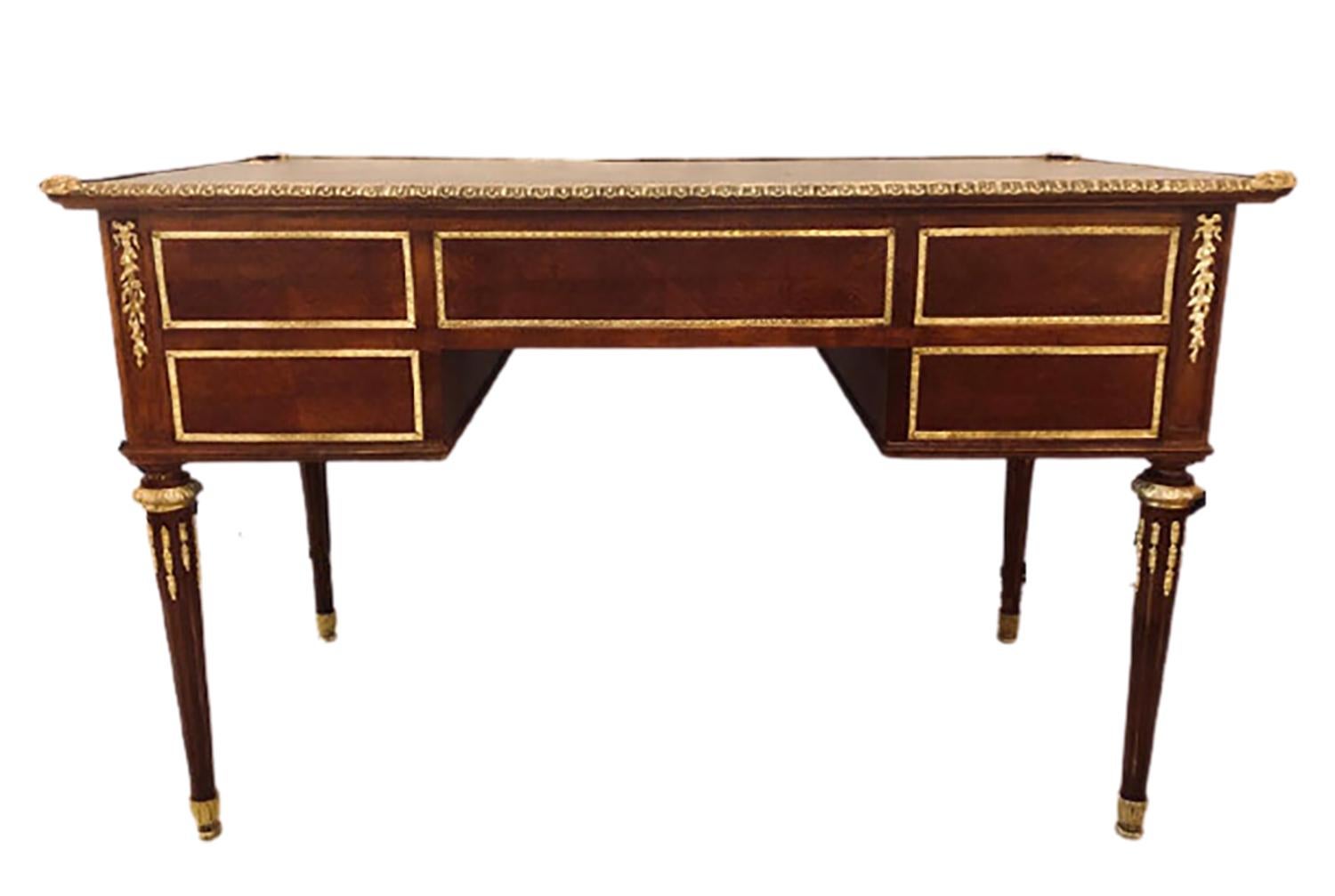 Louis XVI style bronze mounted mahogany writing desk. The tapering Louis XVI style legs having bronze sabots and mountings inside the strong reeded legs which terminate in bronze capitals. The case with a center bronze framed drawer flanked by