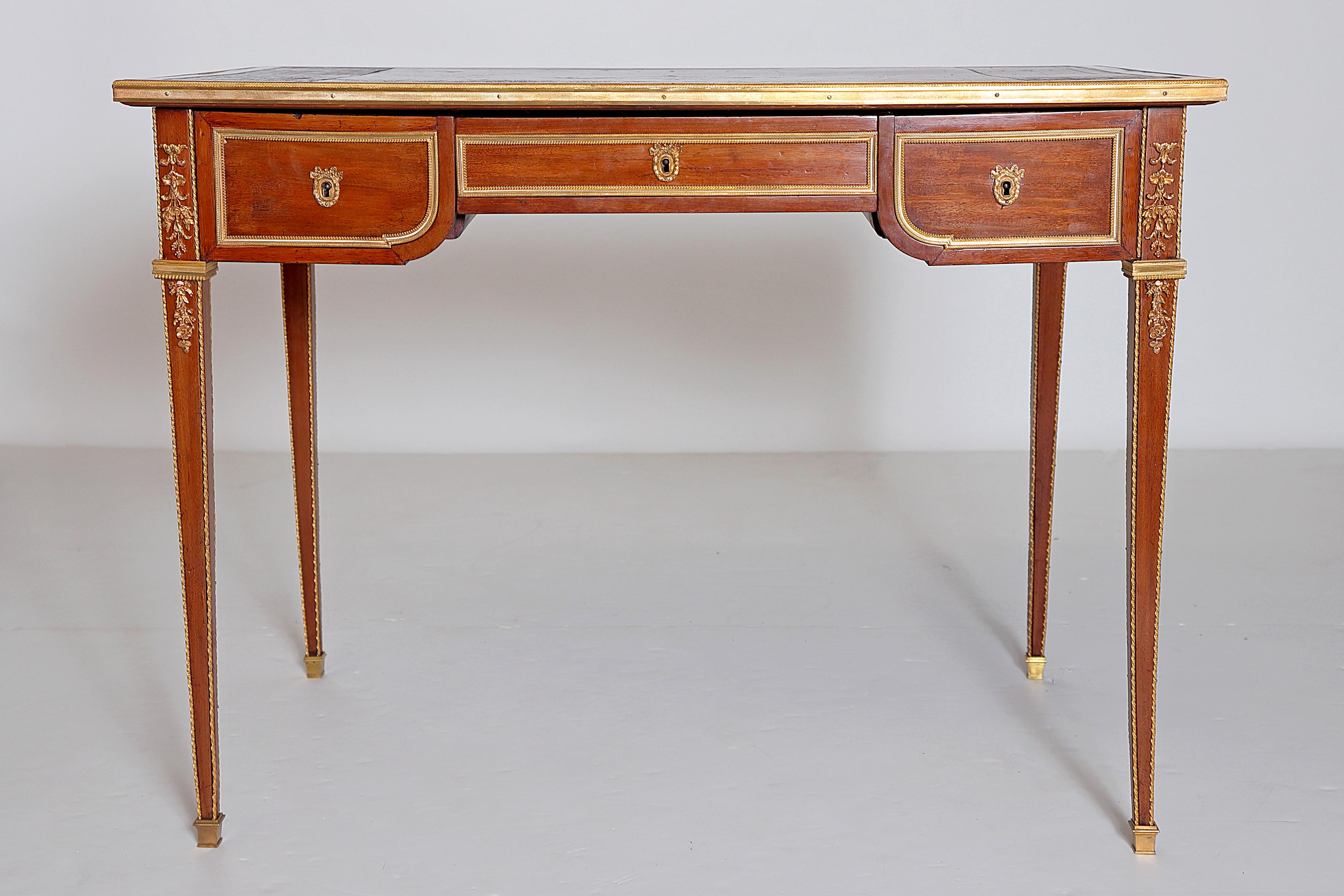A small, elegant Louis XVI style writing table, mahogany with ormolu, dark red leather writing surface with tooled (embossed) gilt trim around the edge and central diamond shaped ornament / design, the whole edge of the table top is trimmed in gilt