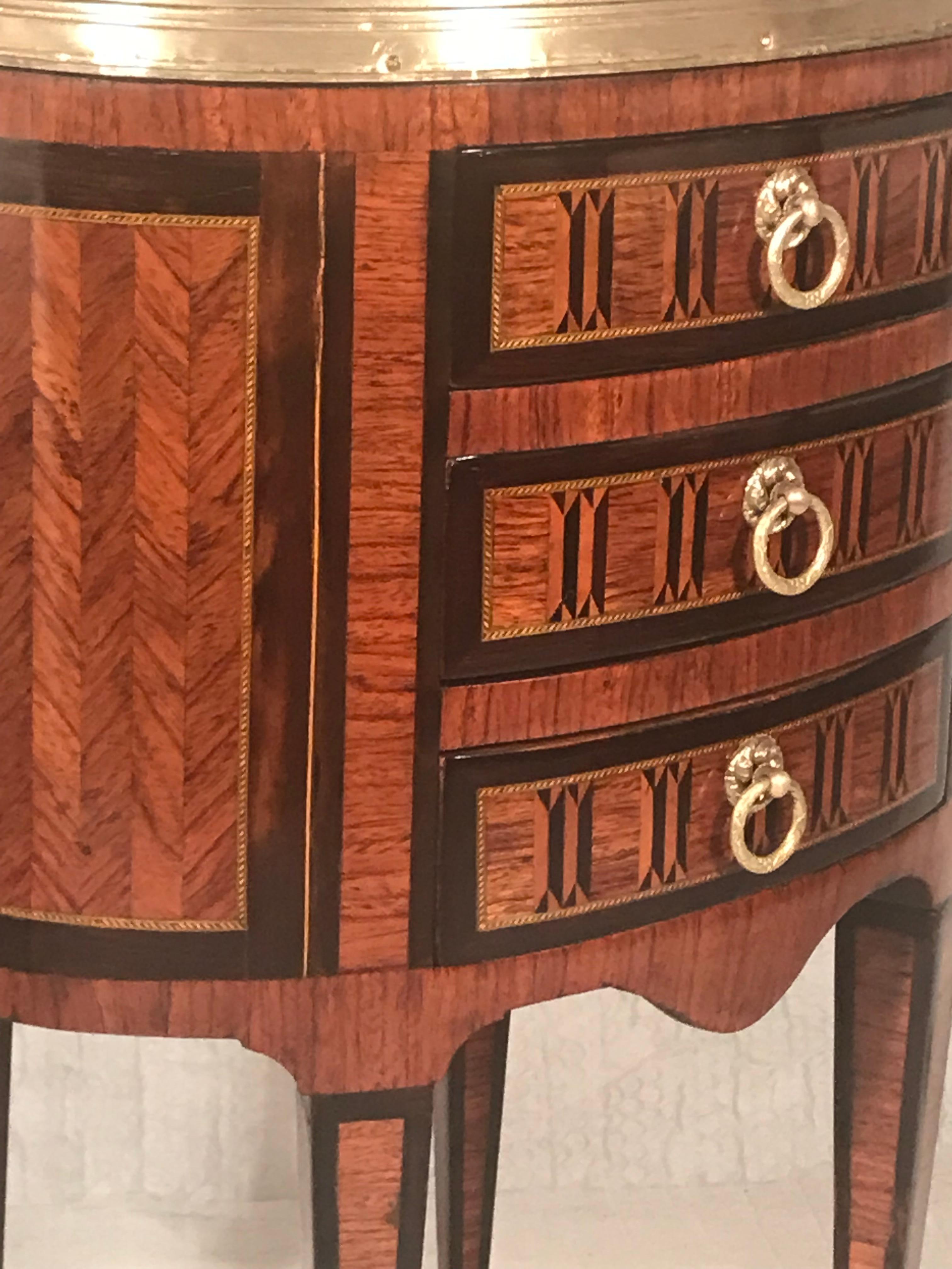 Der Beistelltisch Tambour im Louis XVI-Stil, der für sein exquisites Intarsien-Dekor bekannt ist, ist ein herausragendes Möbelstück. Dieser zeitlose Beistelltisch mit drei Schubladen bietet Funktionalität und Eleganz zugleich und steht auf schlanken