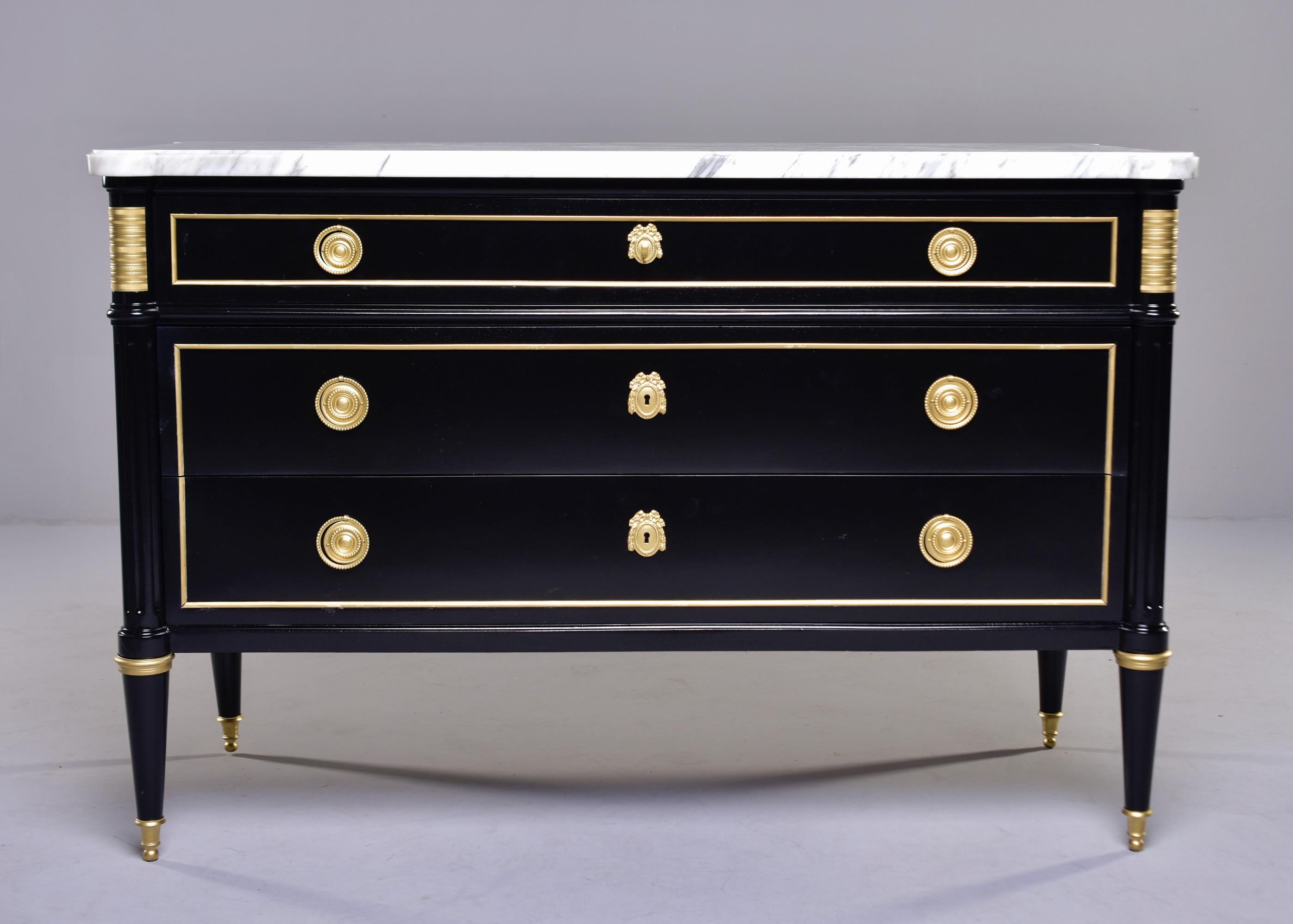 Circa 1920s Louis XVI style three drawer commode in mahogany with new black finish features brass hardware and trim, functional locks and white marble top. Unknown maker.