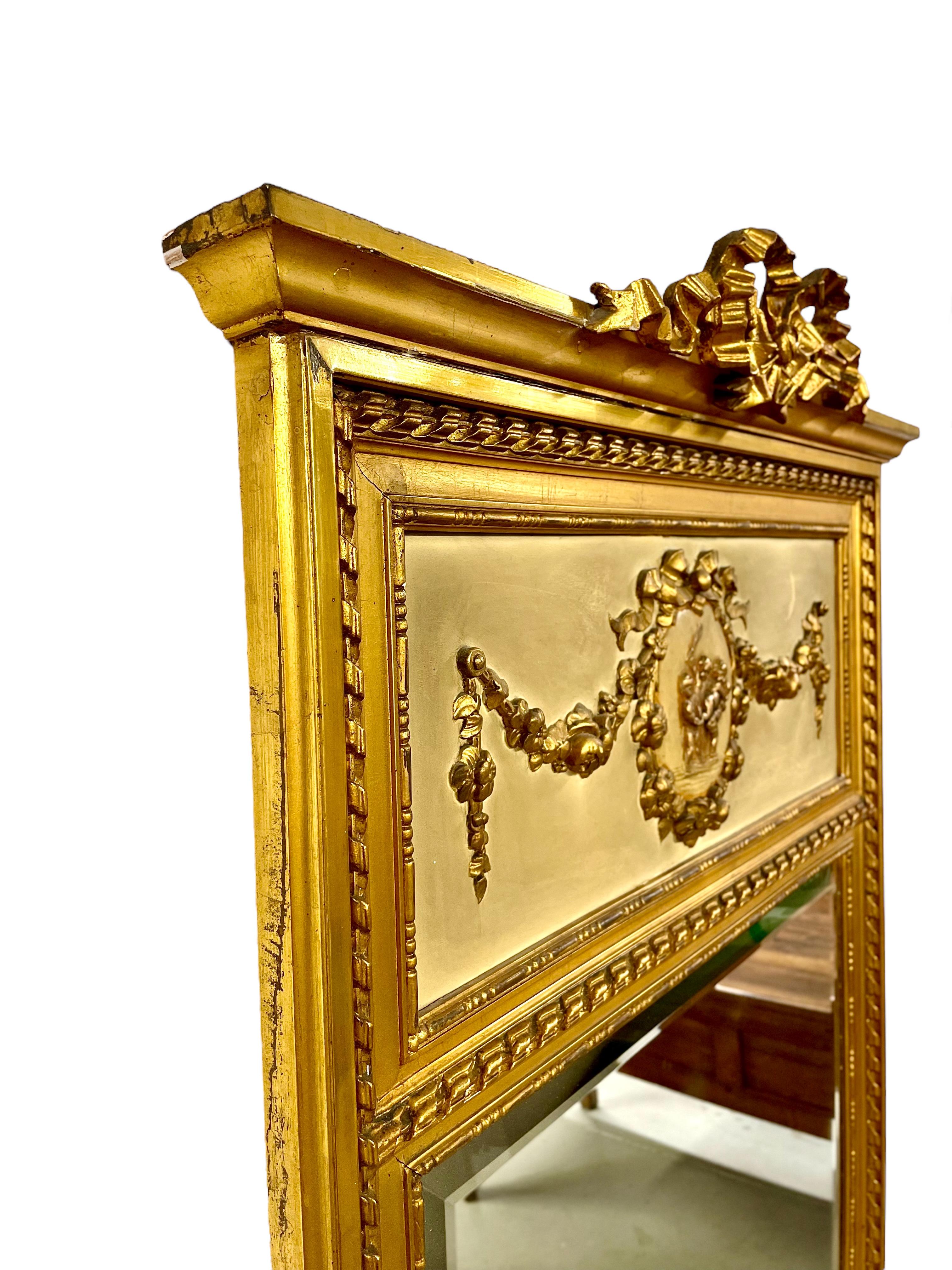 Dieser fabelhafte Trumeau-Spiegel im Louis XVI-Stil ist aus Holz und vergoldetem Stuck gefertigt. Seine abgeschrägte Spiegelplatte ist von einer kunstvoll geschnitzten Umrandung aus drei Perlen und einem gedrehten Seil umgeben. Der obere Teil des
