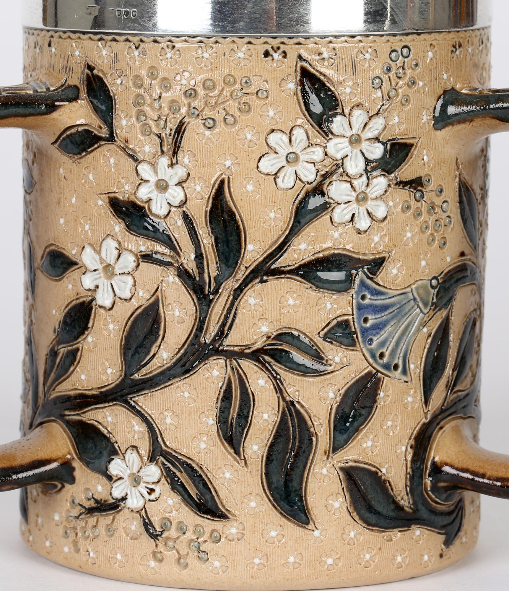 A very fine and stylish Doulton Lambeth silver mounted art pottery three handled tyg descorated with flowering stems by renowned artist Louisa Davis and dated 1878. The rounded cylindrical shaped stoneware tyg has squared off pattern molded handles,
