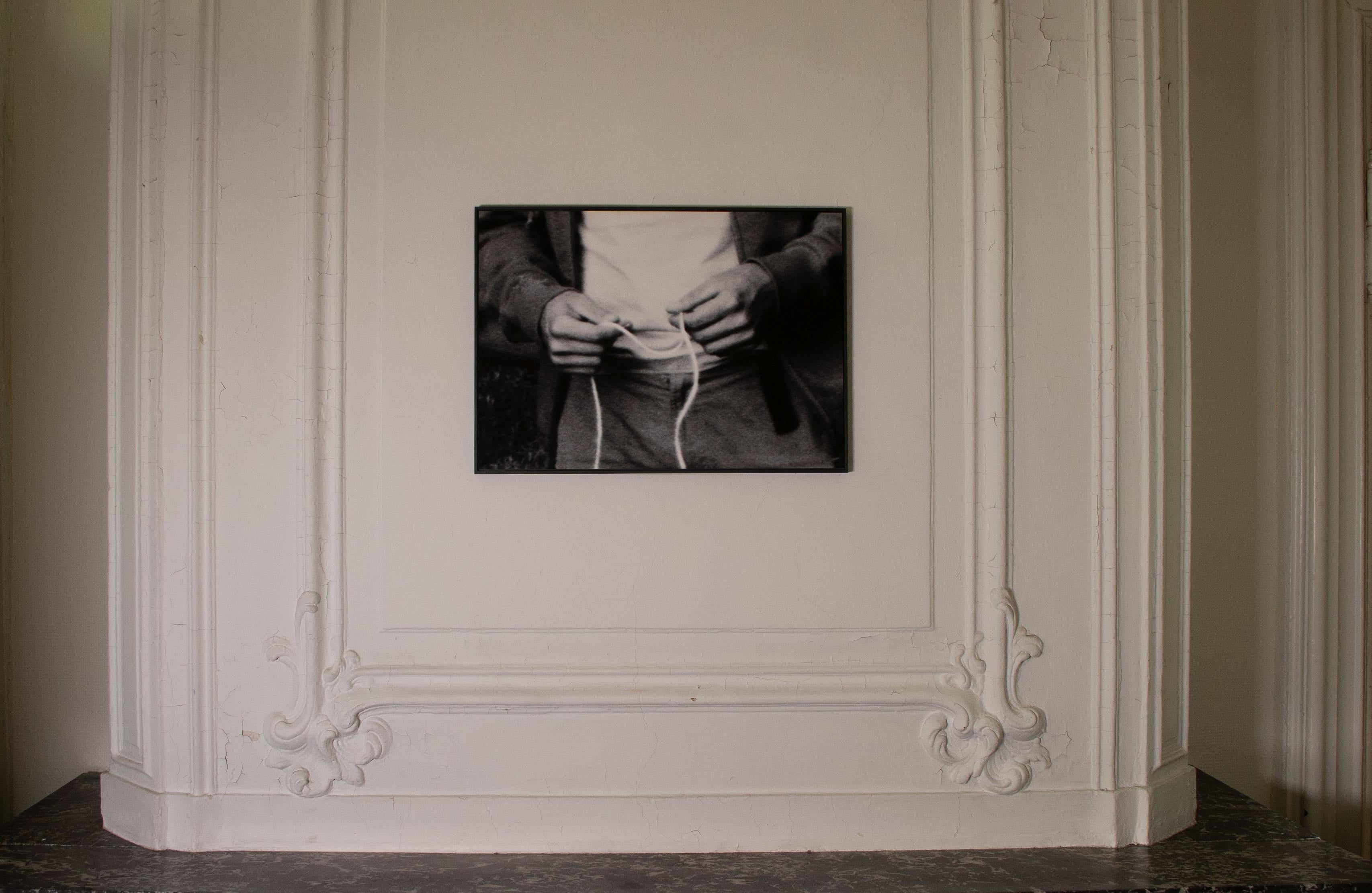 Photo en noir et blanc d'un homme tenant une ficelle, intitulée 'You're wondering why...' (Vous vous demandez pourquoi ?). - Photograph de Louise Degraeve