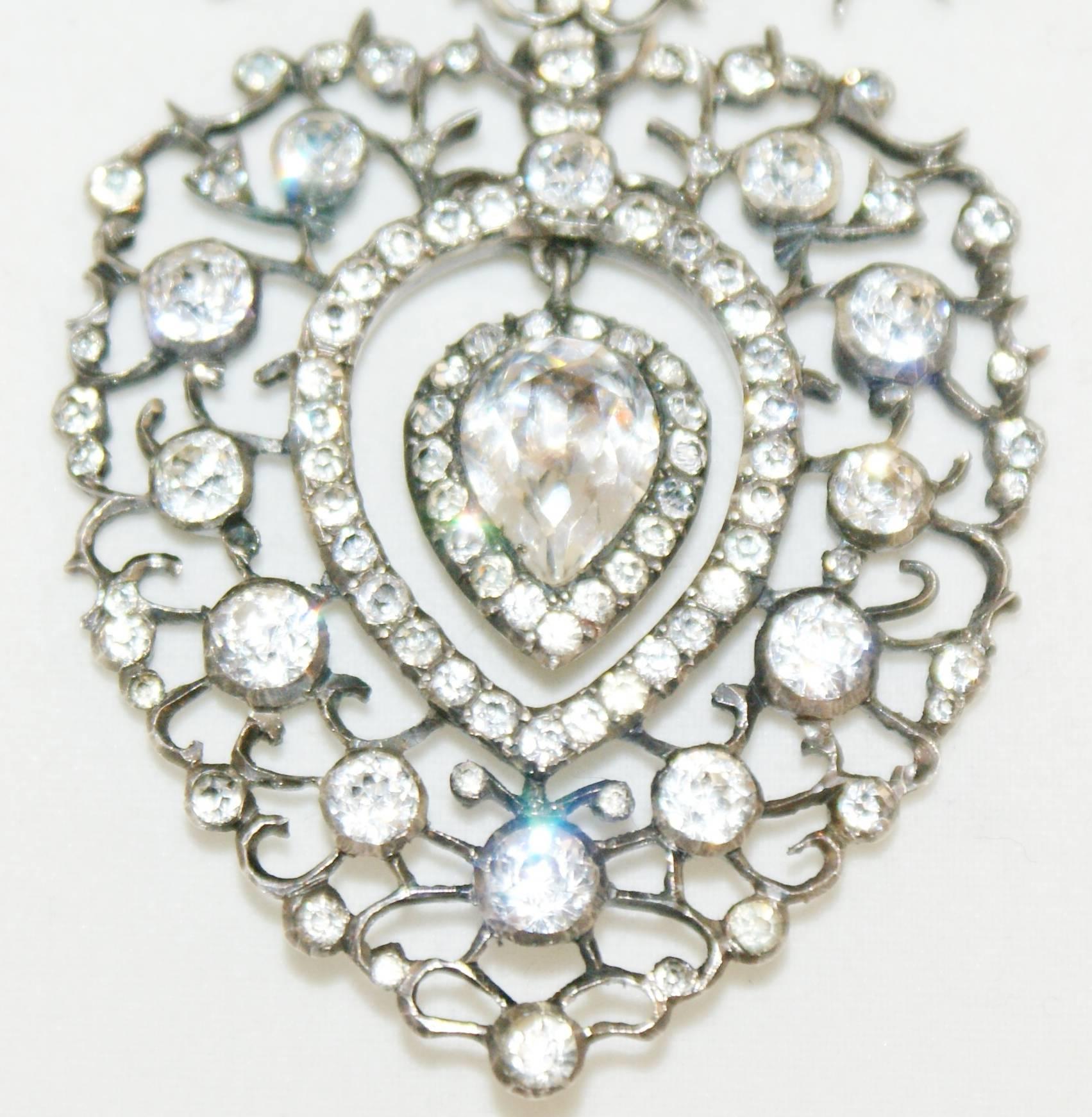 A large and bright antique Louis XVI French paste heart shaped pendant, set in silver. France circa 1780.
The articulated heart pendant is surrounded by a halo and it is suspended from a stylised (descending) dove motif .
It most probably represents