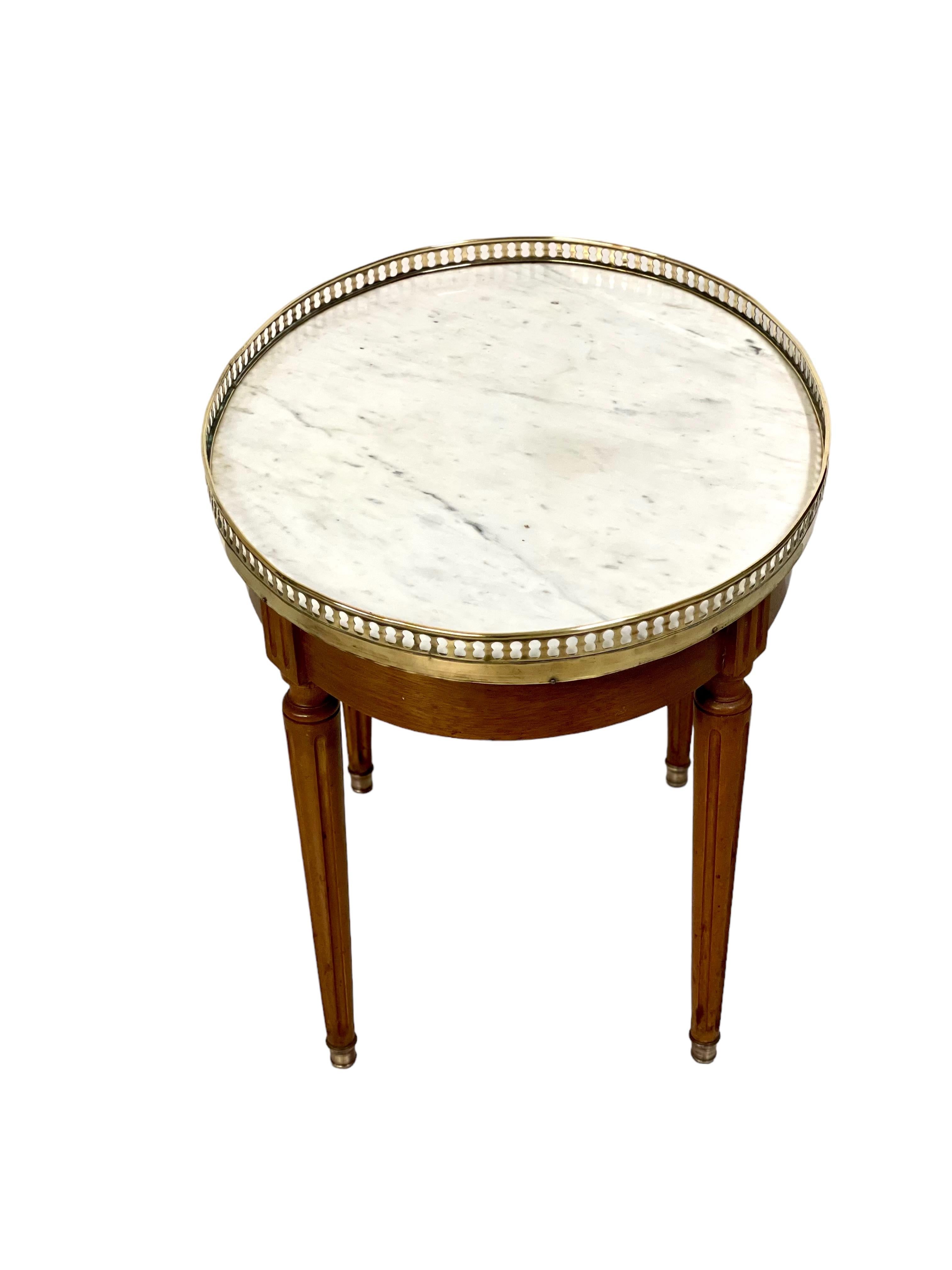 A charming Louis XVI style occasional table featuring an inset circular grey and white veined marble top, with a reticulated brass gallery edge. This oval-shaped table is raised on four turned and tapering fluted legs terminating in brass feet. In