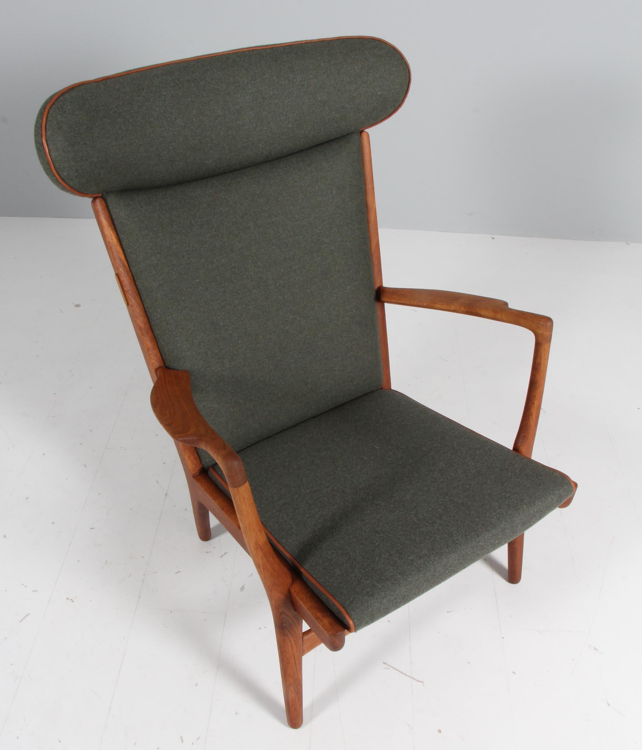 Designed by Hans Wegner in 1951 and produced by A.P. Stolen, this sturdy armchair, model AP15, features an oakframe with a broad curved back and carved armrests. New upholstered with full grain aniline leather details and green wool fabric