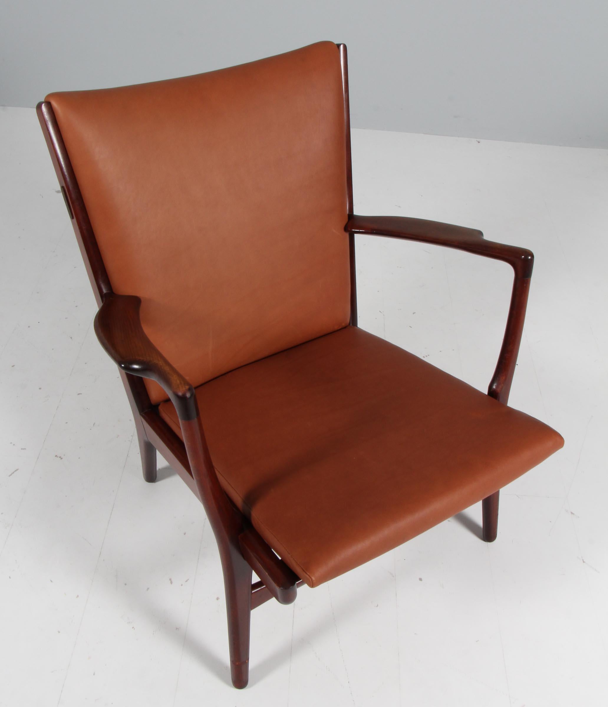Designed by Hans Wegner in 1951 and produced by A.P. Stolen, this sturdy armchair, model AP16, features an beech frame with a broad curved back and carved armrests. New upholstered with full grain aniline leather