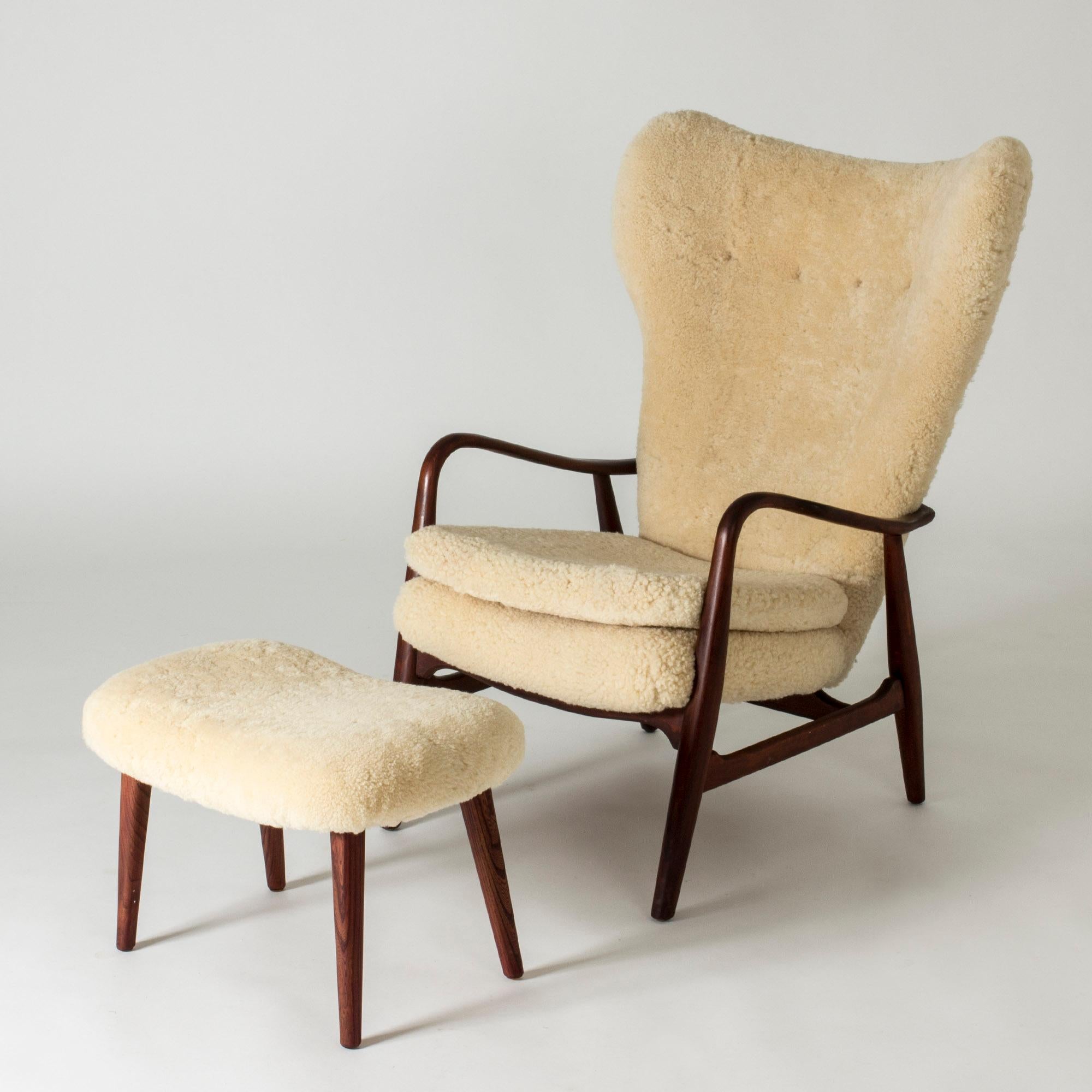 Elegant lounge chair and footstool by Ib Madsen and Acton Schubell, made from rosewood with sheepskin upholstery. Generous size and beautiful wooden details, like the armrests encircling the back.