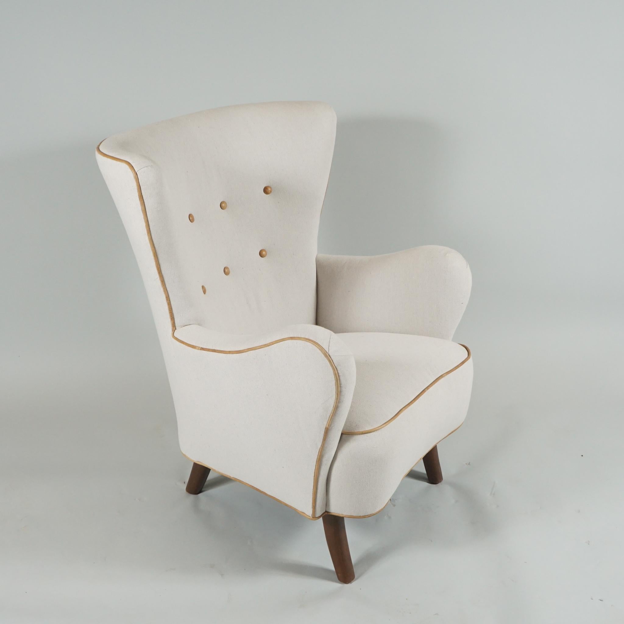 Danish modern upholstered wingback armchair by Danish designer, Alfred Christensen, re-covered in off-white
cotton with buttoned back and piping in beige leather. The generously curved arms and graceful
legs are a signature of this designer.