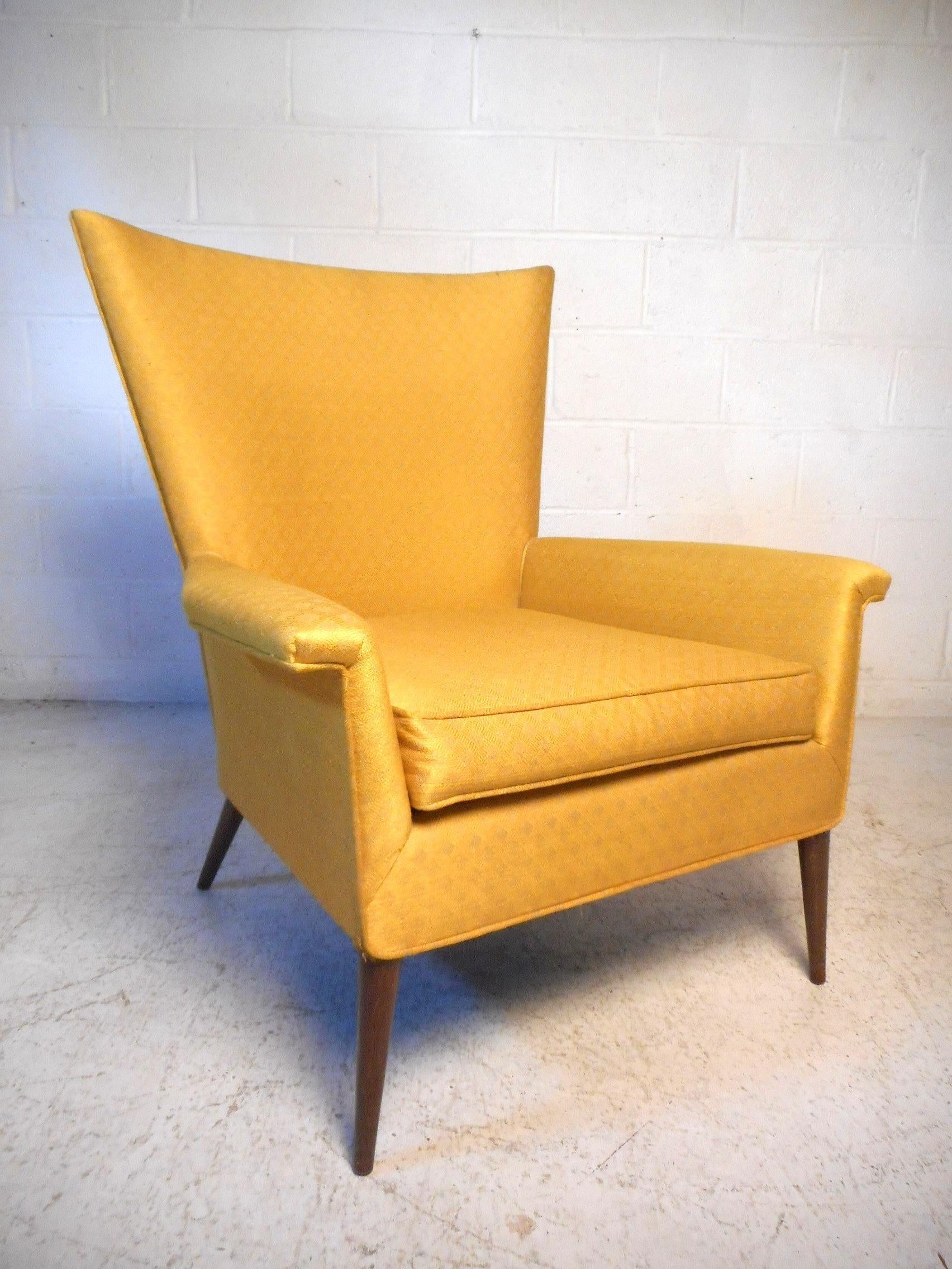 This impressive mid-century lounge chair features a tall winged back, contoured armrests, sleekly splayed and tapered wooden legs, covered with a vibrant yellow upholstery. An exceptional addition to any modern interior's seating arrangement.