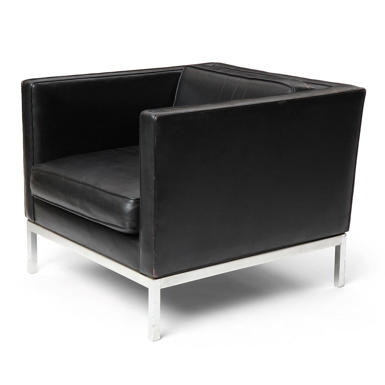 An even arm leather club chair with rectilinear form that floats on a chromed steel base.