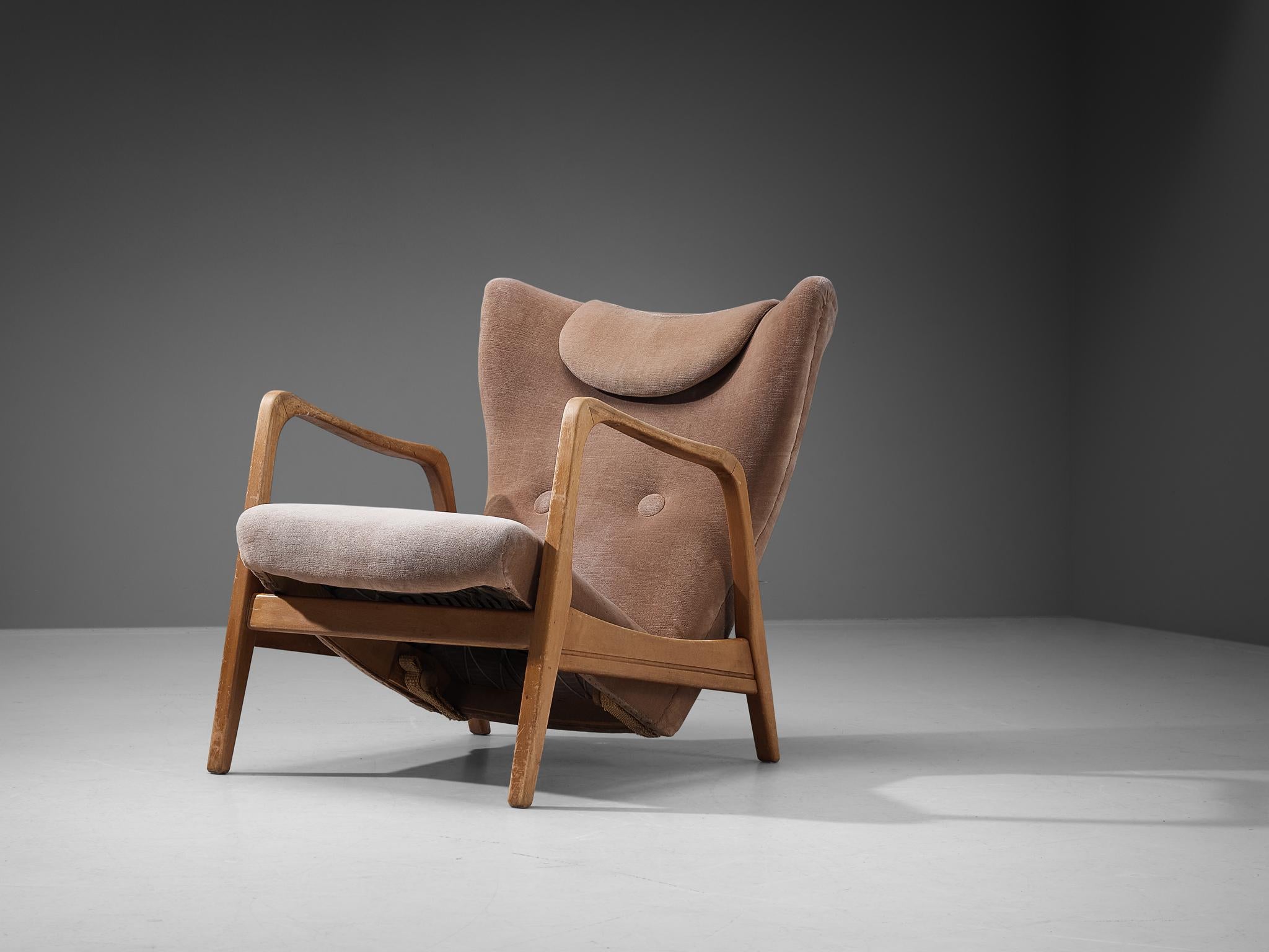 Lounge chair, beech, beige velvet upholstery, Europe, 1960s. 

This comfortable lounge chair features a compelling deep seat that provides the ultimate relaxation. Complemented with a head pillow hanging over the wingback shaped backrest, all