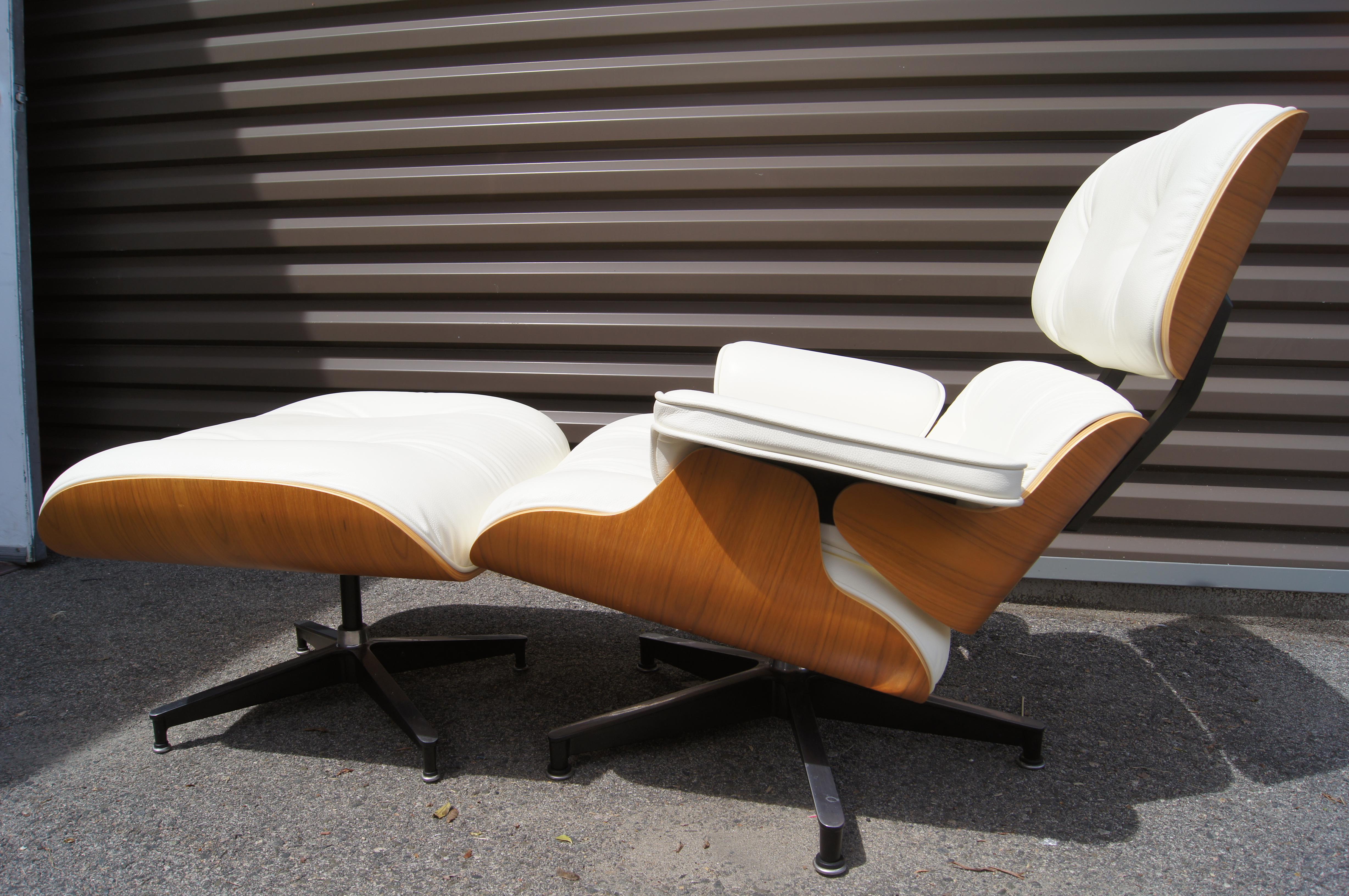 This version of Charles and Ray Eames's iconic molded plywood lounge chair for Herman Miller, model 670/671, features a walnut shell and pearl white leather upholstery. The chair's angled tilt, swiveling base, and matching ottoman offer the deepest