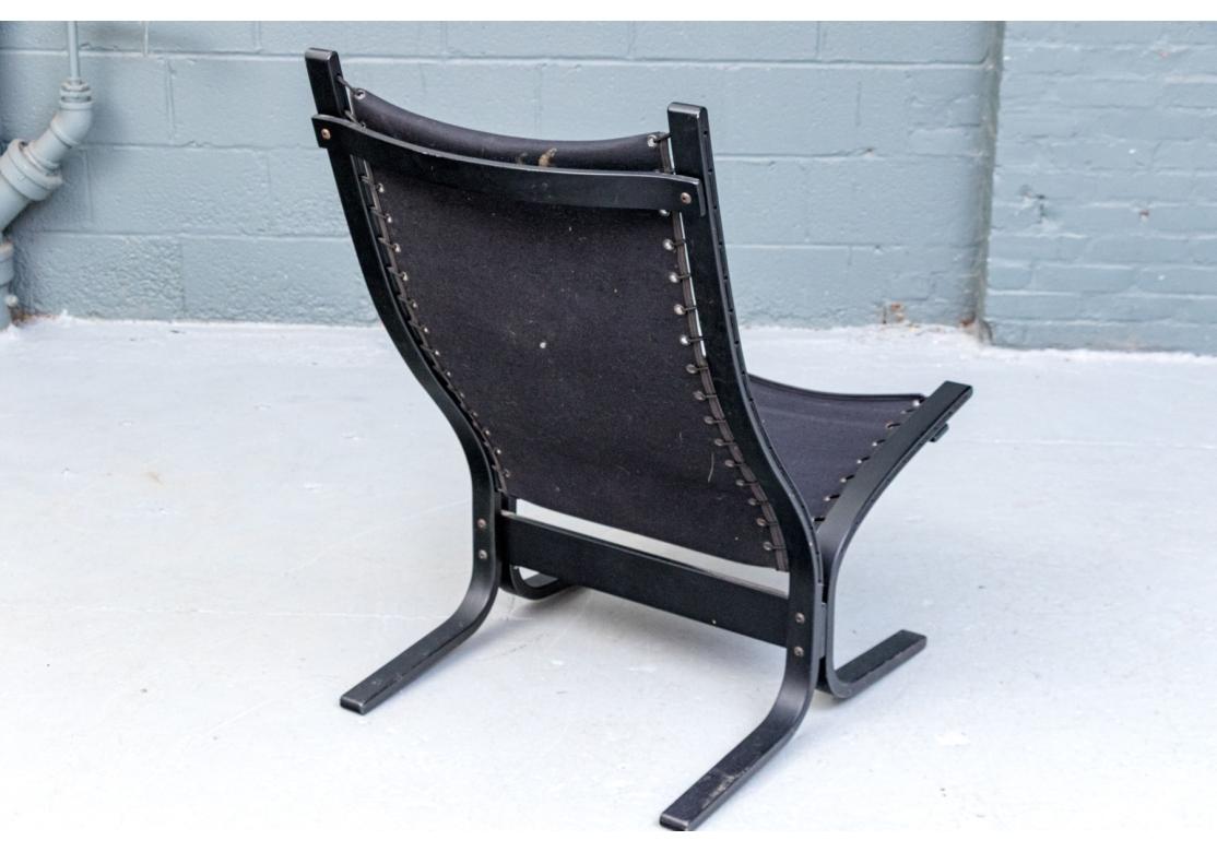 La silueta presenta líneas suaves y orgánicas y una base en voladizo. El armazón de madera curvada en negro y atado con una eslinga de lona con ojales. La silla está revestida con un acolchado de suave piel natural cosida a canal y tela roja