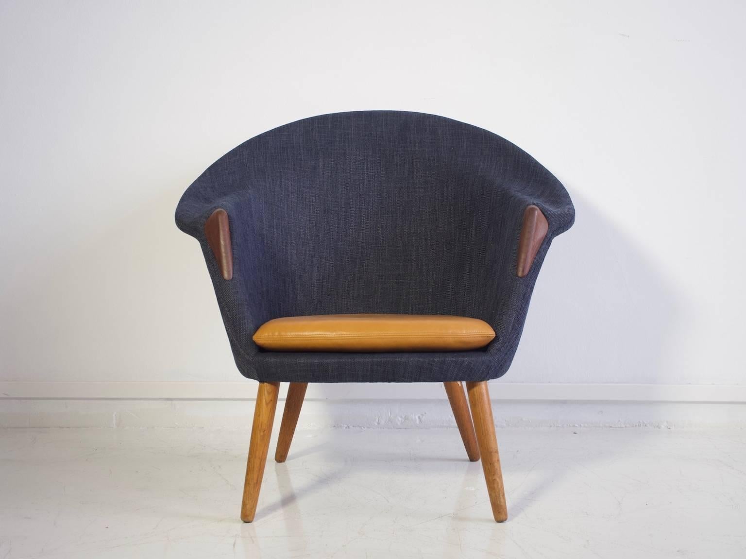 Lounge chair with rounded back set on round tapered legs made of solid oak. Later upholstery in dark blue fabric with armrest details in teak. Loose seat cushion upholstered in silk-aniline leather.