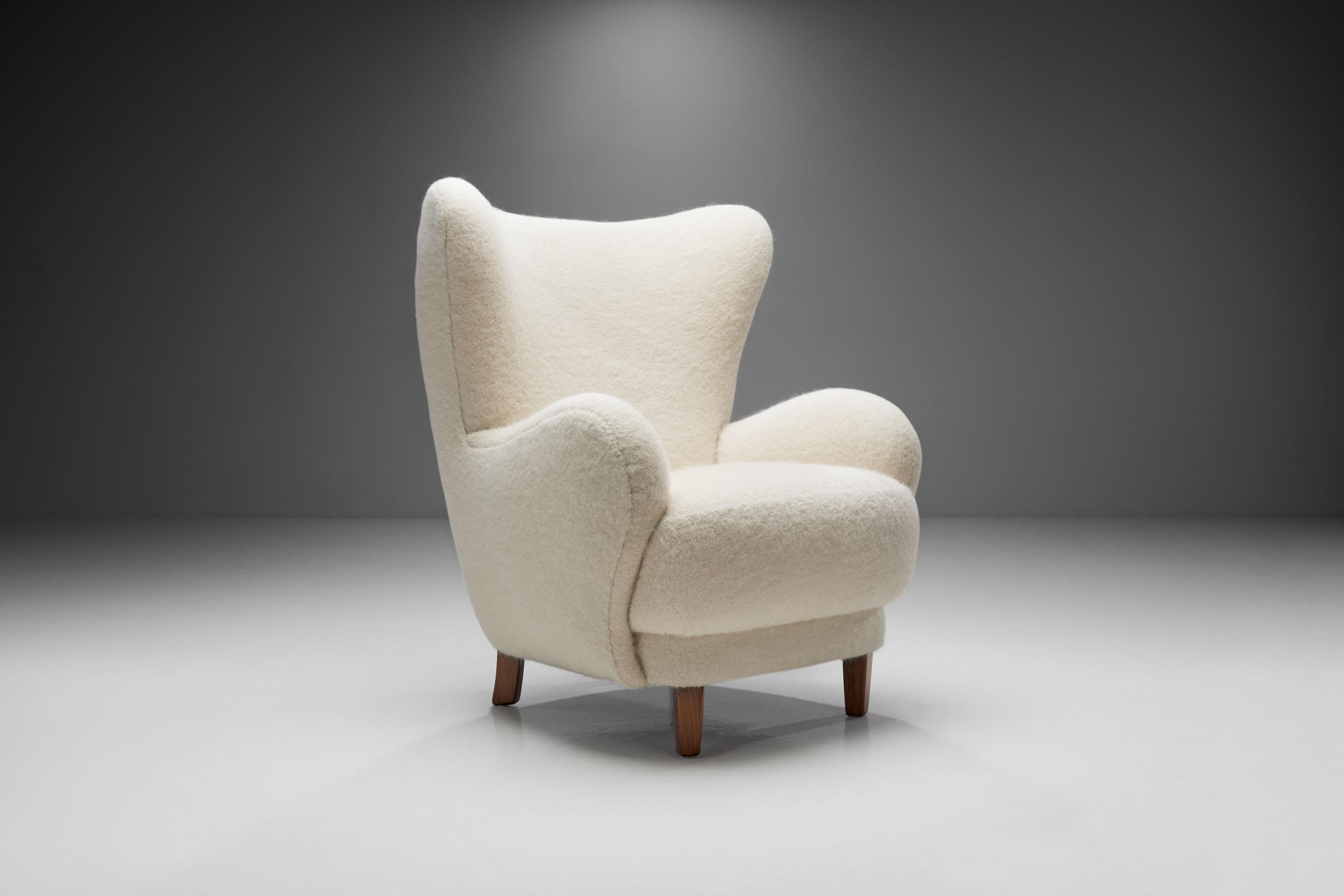 This unique 1940s winged easy chair is a great representation of the quality and craftsmanship of Danish master cabinetmakers and the immediately recognizable characteristics of Scandinavian design. 

The welcoming, rounded shape of the voluminous