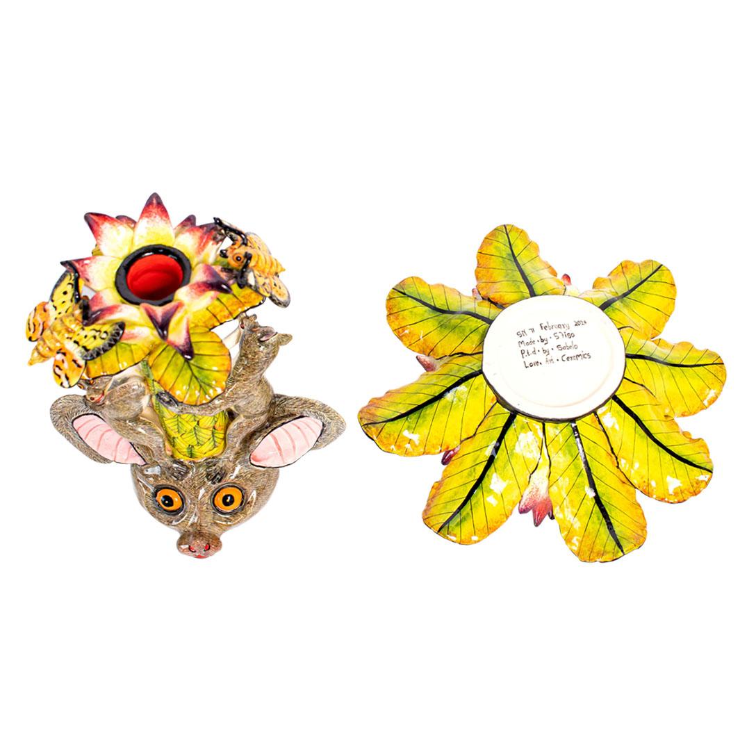 El candelabro de cerámica Bushbaby de Love Art Ceramic, esculpido a mano por Sfiso Mvelase y pintado por Sabelo Nene, es una vibrante celebración de la flora y la fauna sudafricanas. La pieza presenta una base de flor de protea esculpida a mano en