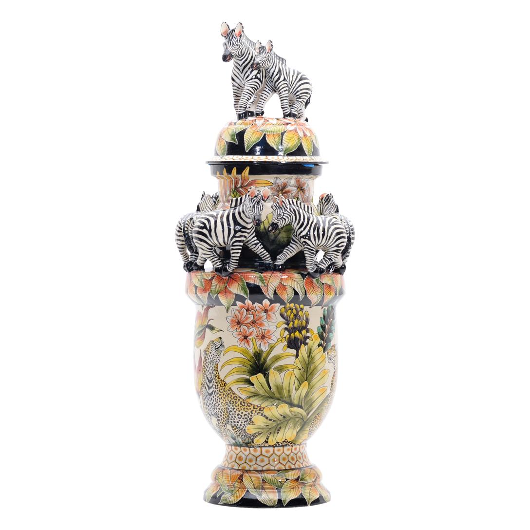 Introducing the Zebra Urn, a creation by Love Art Ceramic in South Africa. This piece was sculpted by Motsamai Sello and hand-painted by Nozipho Ntshalintshali. It measures H.24 in. L.6 in. W.6 in. The Zebra Urn encapsulates the essence of South