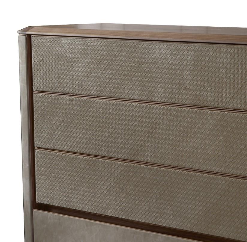 This exquisite chest of drawers features a structure in walnut with a top in walnut-veneered wood. The sides, with delicate round angles and the front panels of the drawers are upholstered in leather of the same walnut color. The leather covering
