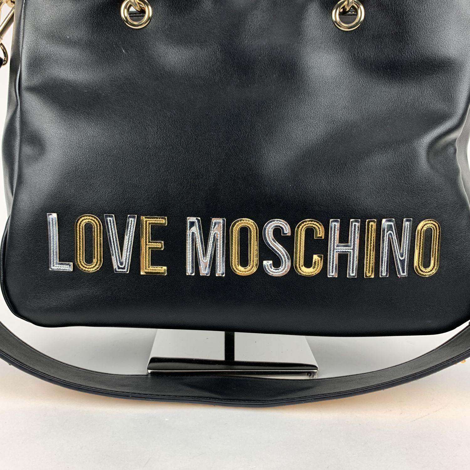 Love Moschino black tote bag with gold and silver logo lettering on the front. It features double handles and removable shoulder strap, with gold-tone sequin strap. Upper zipper closure. Red satin lining. 1 side zip pocket and 1 side open pocket