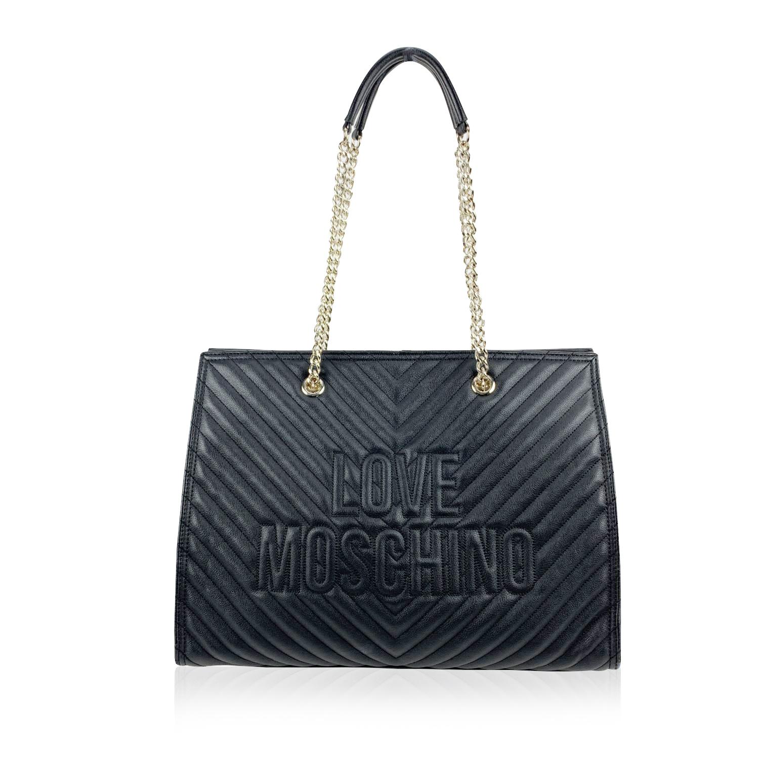 Love Moschino black leather-look canvas tote bag with chevron quilting. It features double chain and leather strap, 'Love Moschino' logo on the front and magnetic button closure on top. Red satin lining. 1 middle zip section and 2 side pockets.