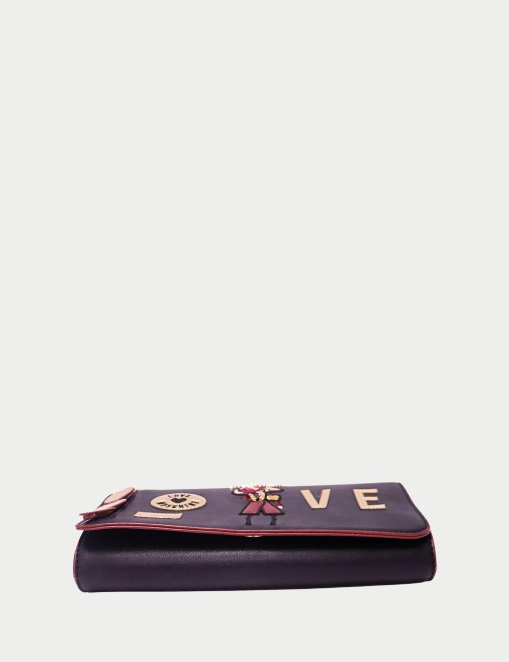 Élevez votre style avec ce sac à main à rabat noir Love Moschino, un mélange chic de design ludique et de praticité au quotidien.

Confectionné en similicuir lisse, il présente des détails appliqués audacieux avec le mot LOVE et les accents du logo