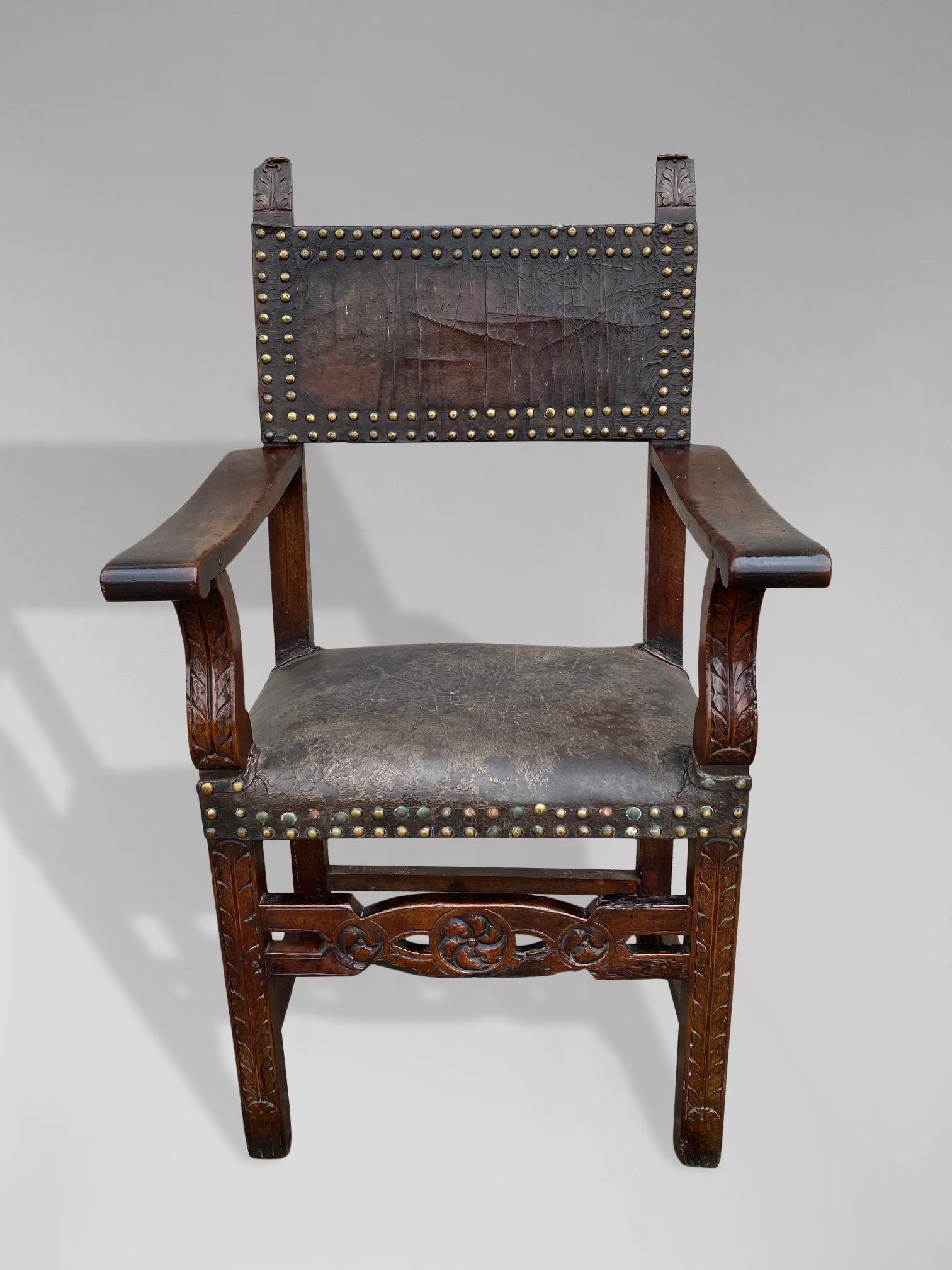 A lovely late 17th century Spanish walnut and leather armchair, retaining its original leather seat and back, held by worn gilt brass studs. The back of the chair has two finely carved scroll acanthus finials above two broad arms, which are