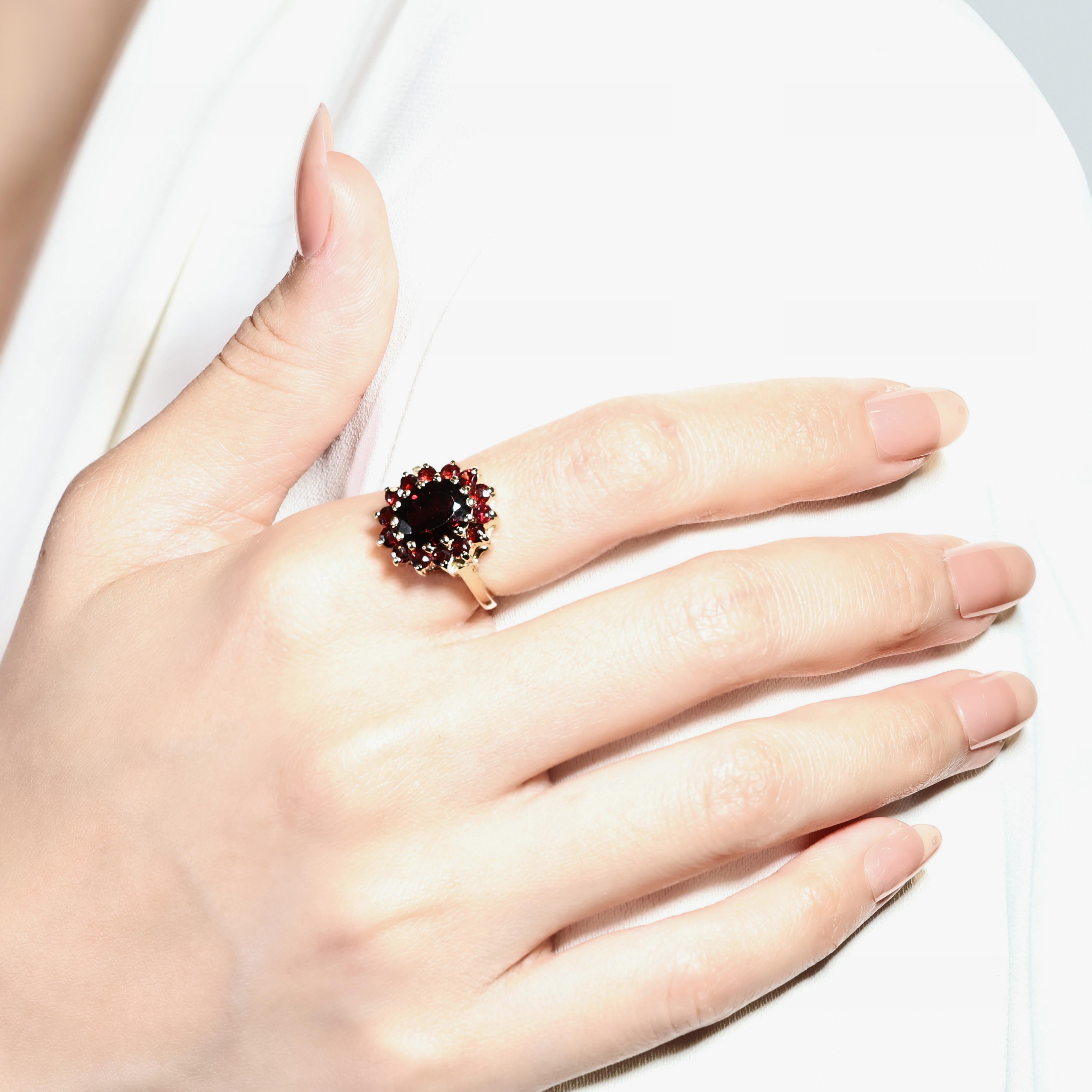 Ce bijou exquis est fabriqué en or jaune 14 carats et présente un magnifique grenat de forme ovale comme pierre principale, pesant 2,01 carats. La teinte rouge vibrante du grenat principal est magnifiquement complétée par 14 autres grenats ronds et
