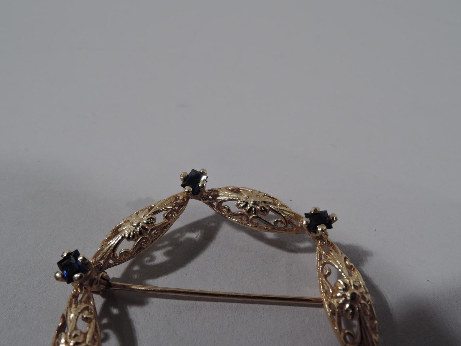 Lovely 14K gold and sapphire pin. Pierced floral wreath interspersed with 6 square-cut sapphires. United States, ca 1930s.