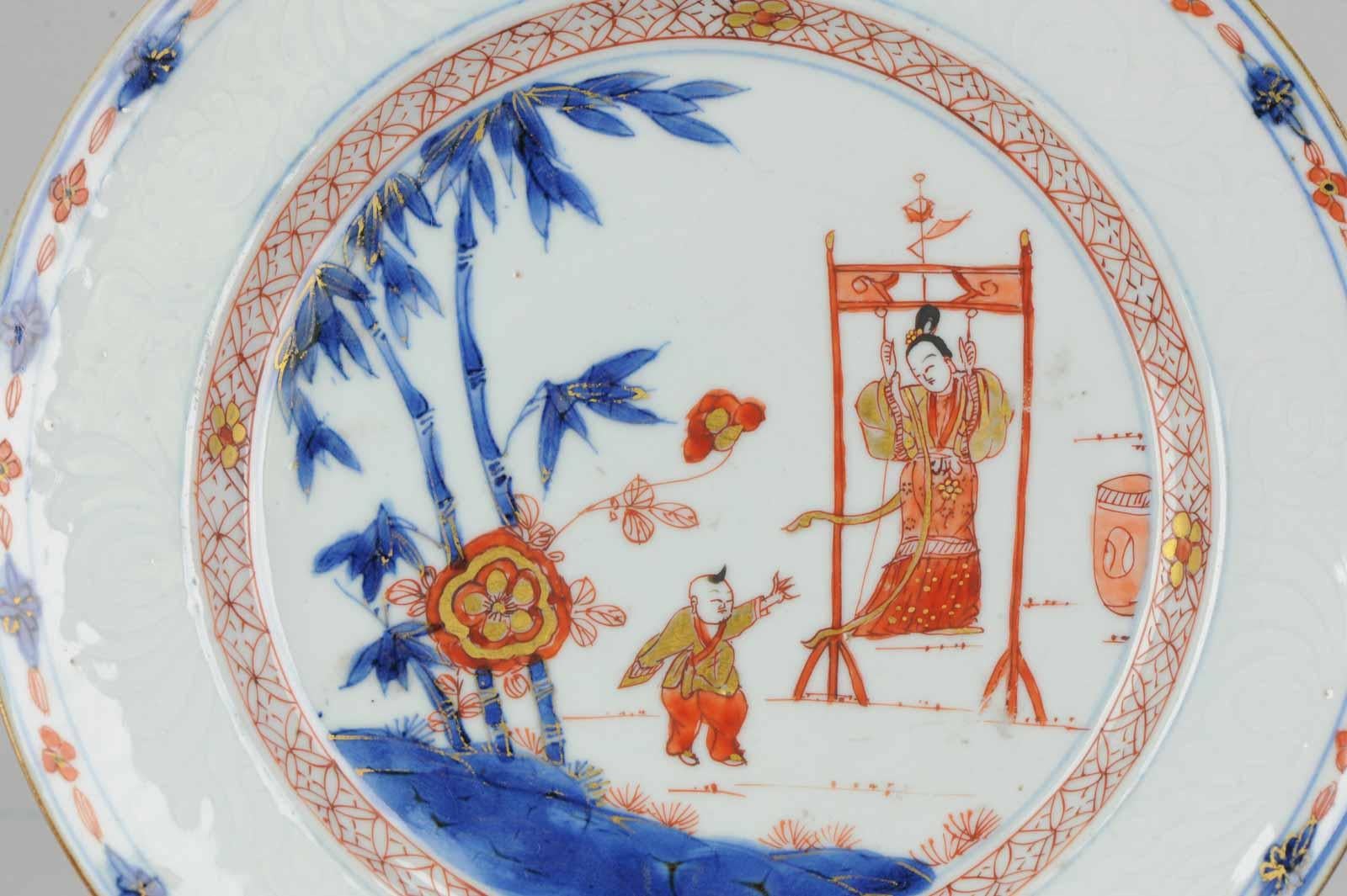 Dish on footring with a flat, underglaze brown-edged, rim (jia mangkou). Chinese Imari, decorated in underglaze blue, overglaze iron-red, black and gold. In the centre a Chinese garden scene with a flowering peony plant and a large bamboo tree with