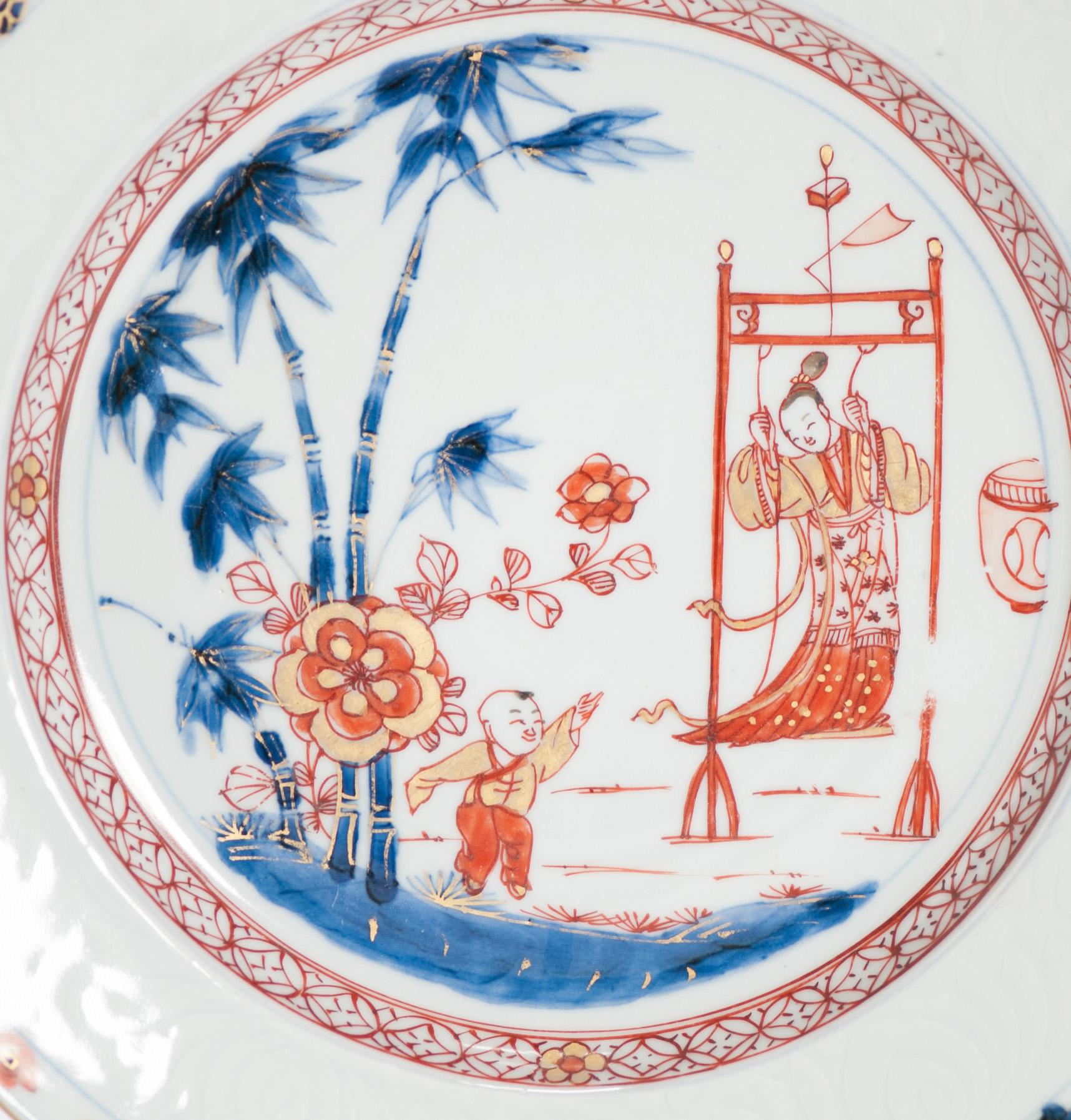 Dish on footring with a flat, underglaze brown-edged, rim (jia mangkou). Chinese Imari, decorated in underglaze blue, overglaze iron-red, black and gold. In the centre a Chinese garden scene with a flowering peony plant and a large bamboo tree with