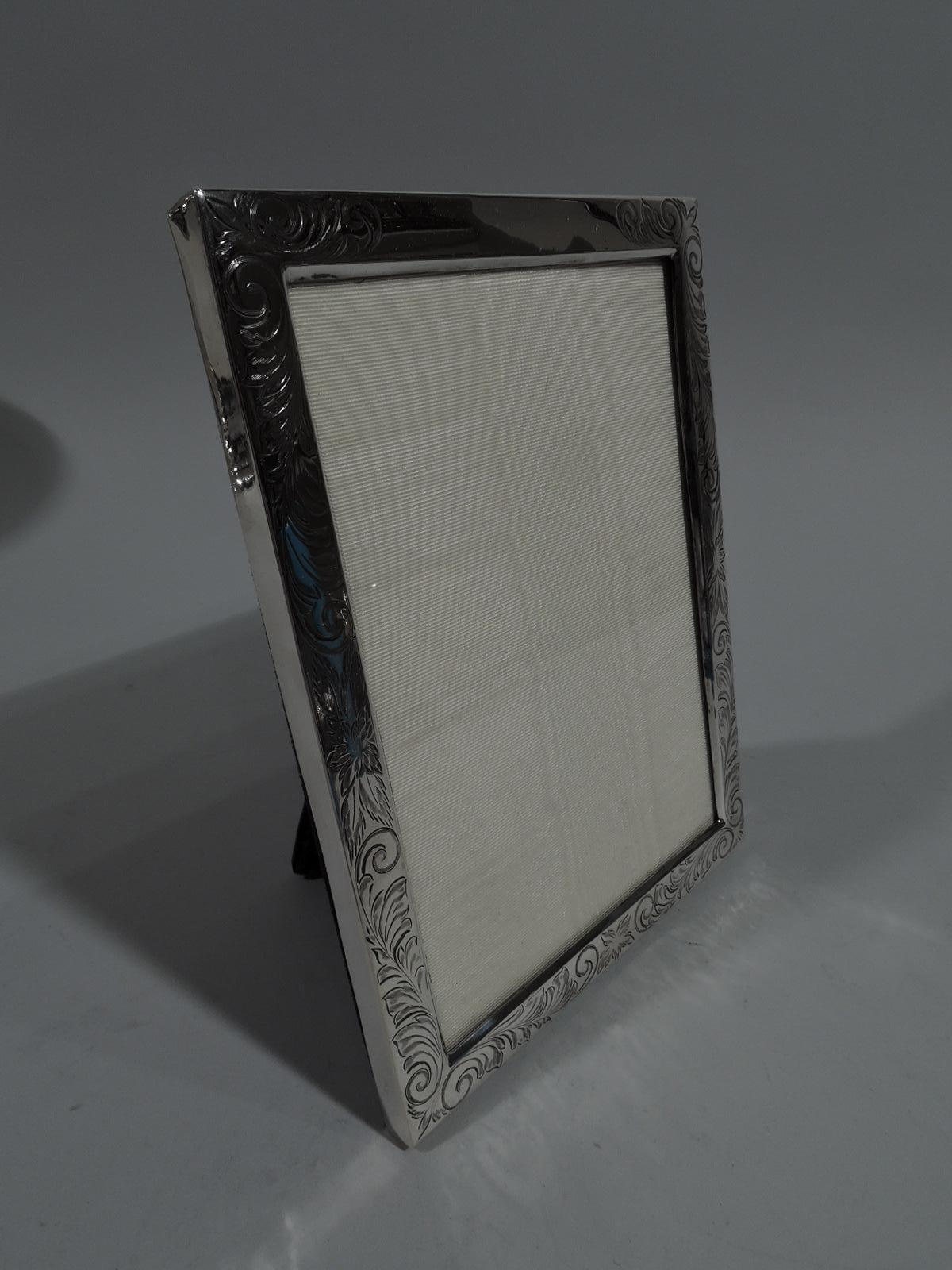 Lovely Art Nouveau sterling silver picture frame. Rectangular window and flat surround engraved with delicate and fluid scrolls and flowers. Center top rail vacant. With glass, silk lining and velvet back and hinged support. Fully marked including