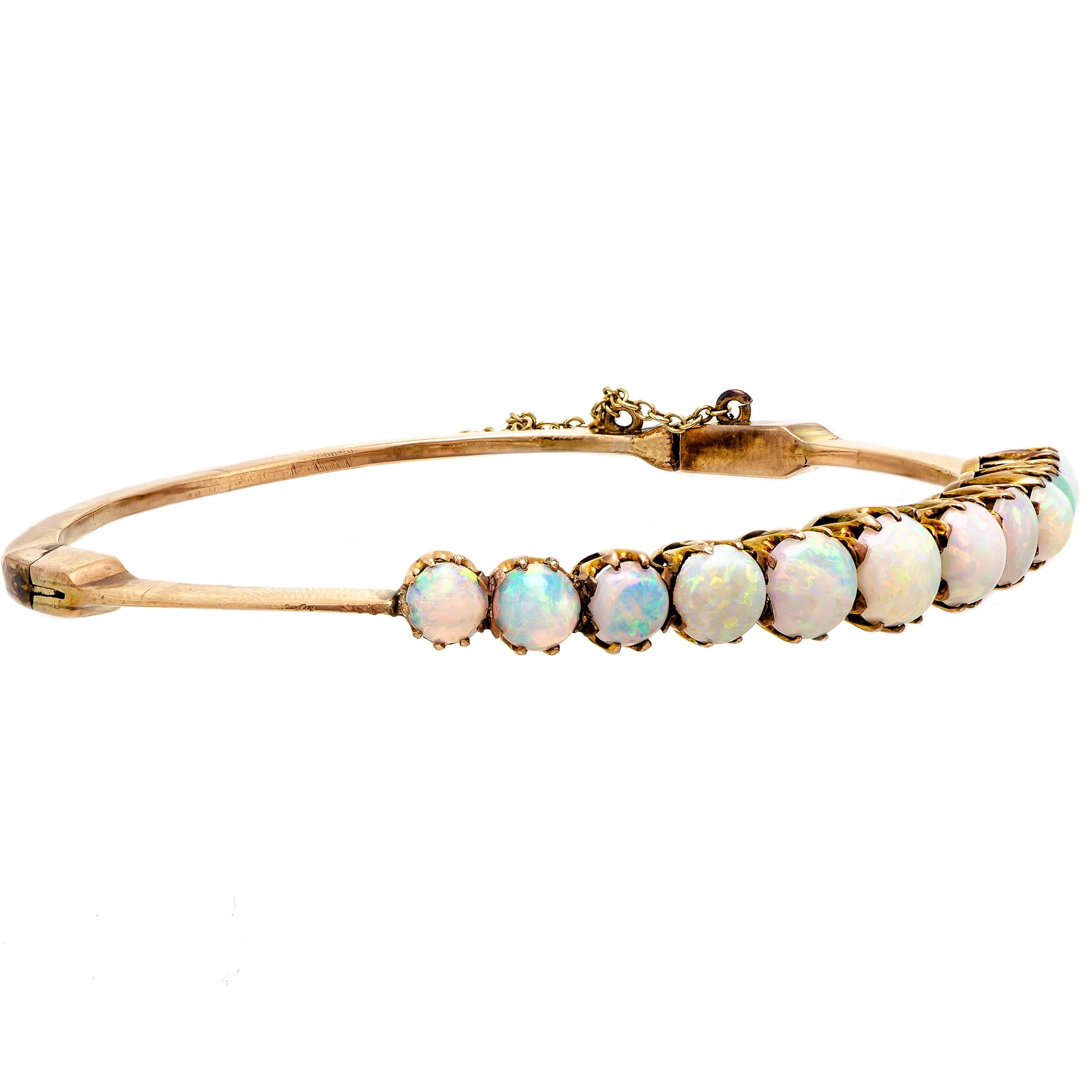 An exquisite antique circa 1900 opal and yellow gold stiff-hinged, half hoop bangle bracelet. Set with 11 round, vibrant graduating opals ranging in size from approximately 5.5 mm to 7.5 mm. These opals are prong set into basket mountings. This