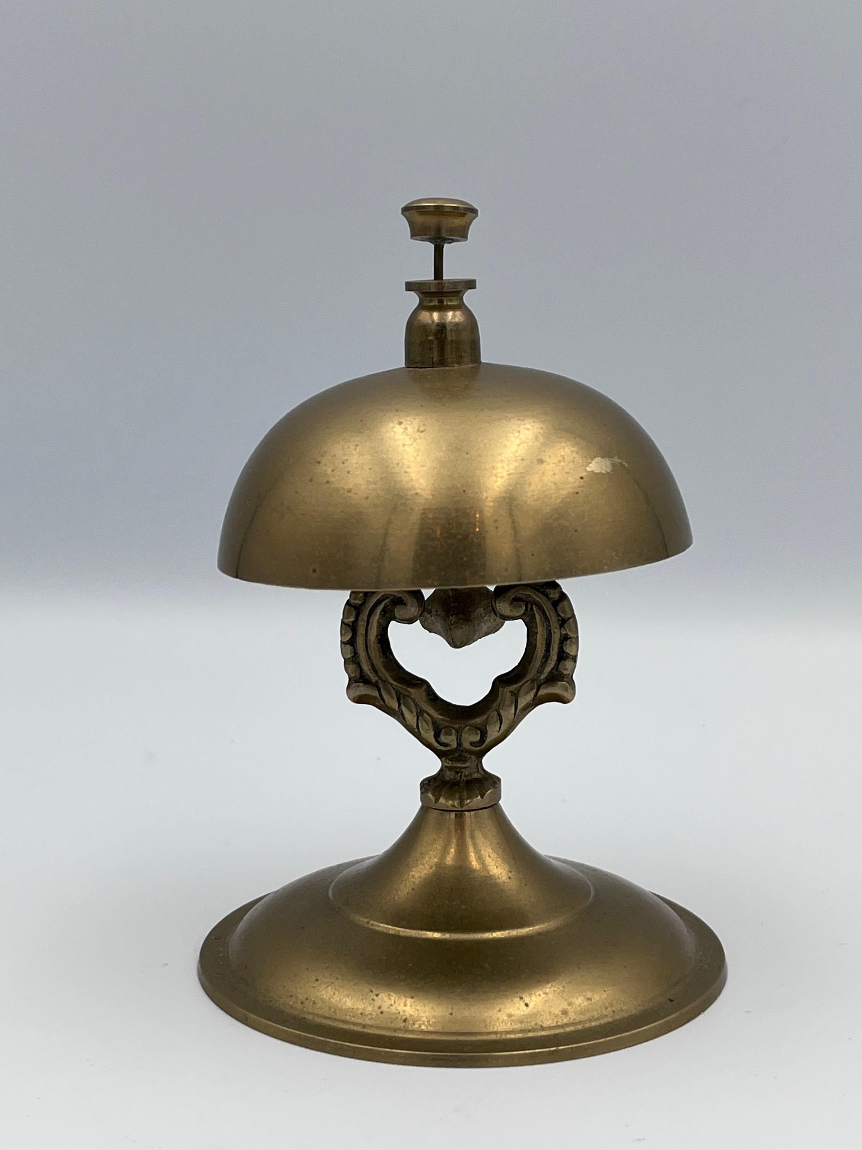 Cloche de comptoir ou de service en laiton Vintage 

Cette cloche de comptoir vintage en laiton est une pièce de belle facture, dotée d'un support simple en forme de harpe sur une base large et stable. Conçue pour être à la fois élégante et durable,