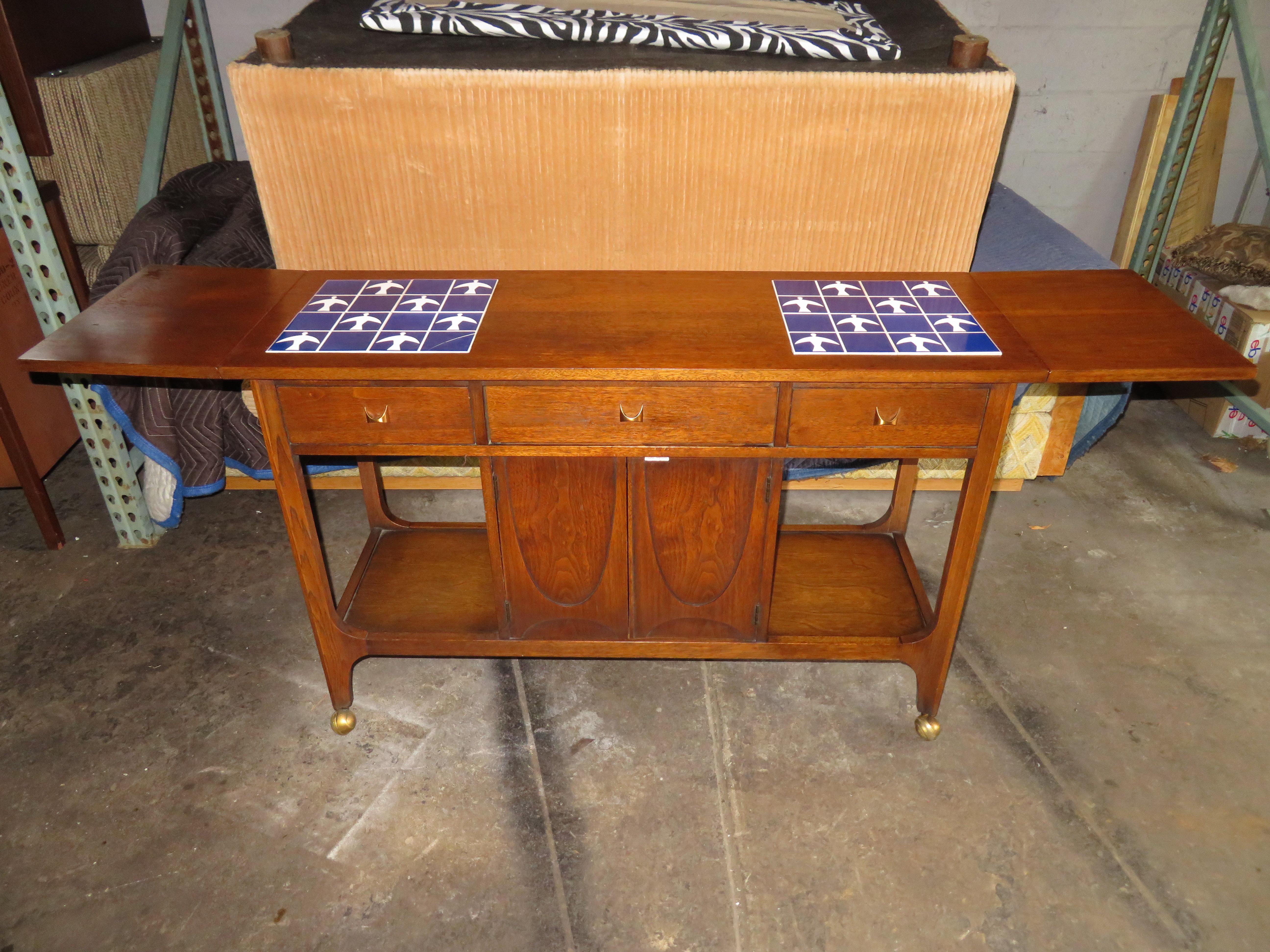 Lovely Broyhill Brasilia drop leaf tile top serving bar cart console table. We love that this piece has the wonderful original blue and white flying bird tiles-one has a small crack-hard to notice. This versatile piece has cabinet space for bottles