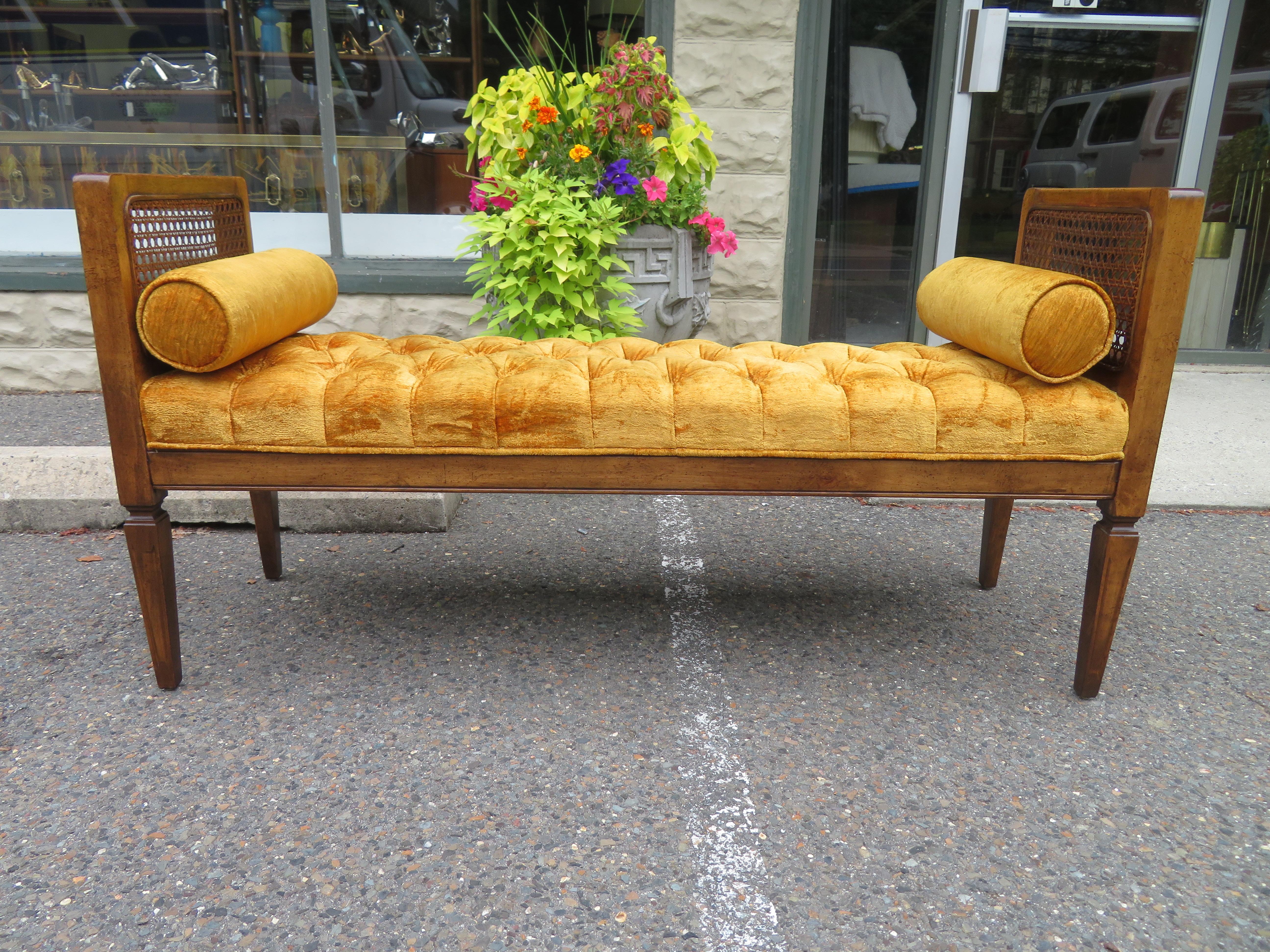 Lovely caned walnut bench with original tufted gold velvet upholstery. We love the original cylinder pillows that flank each end along with the lightly distressed original finish.