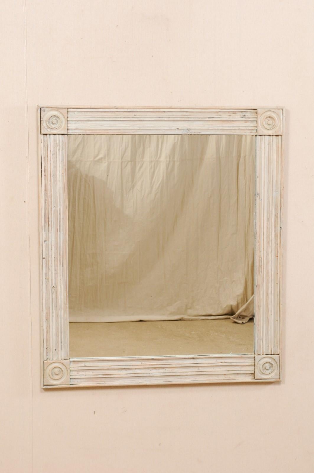A vintage American carved and painted wooden mirror. This American mirror, from the mid-20th century, features a reeded wood surround which is accented at each corner with circular carved medallions. The mirror frame has a natural pale wood base