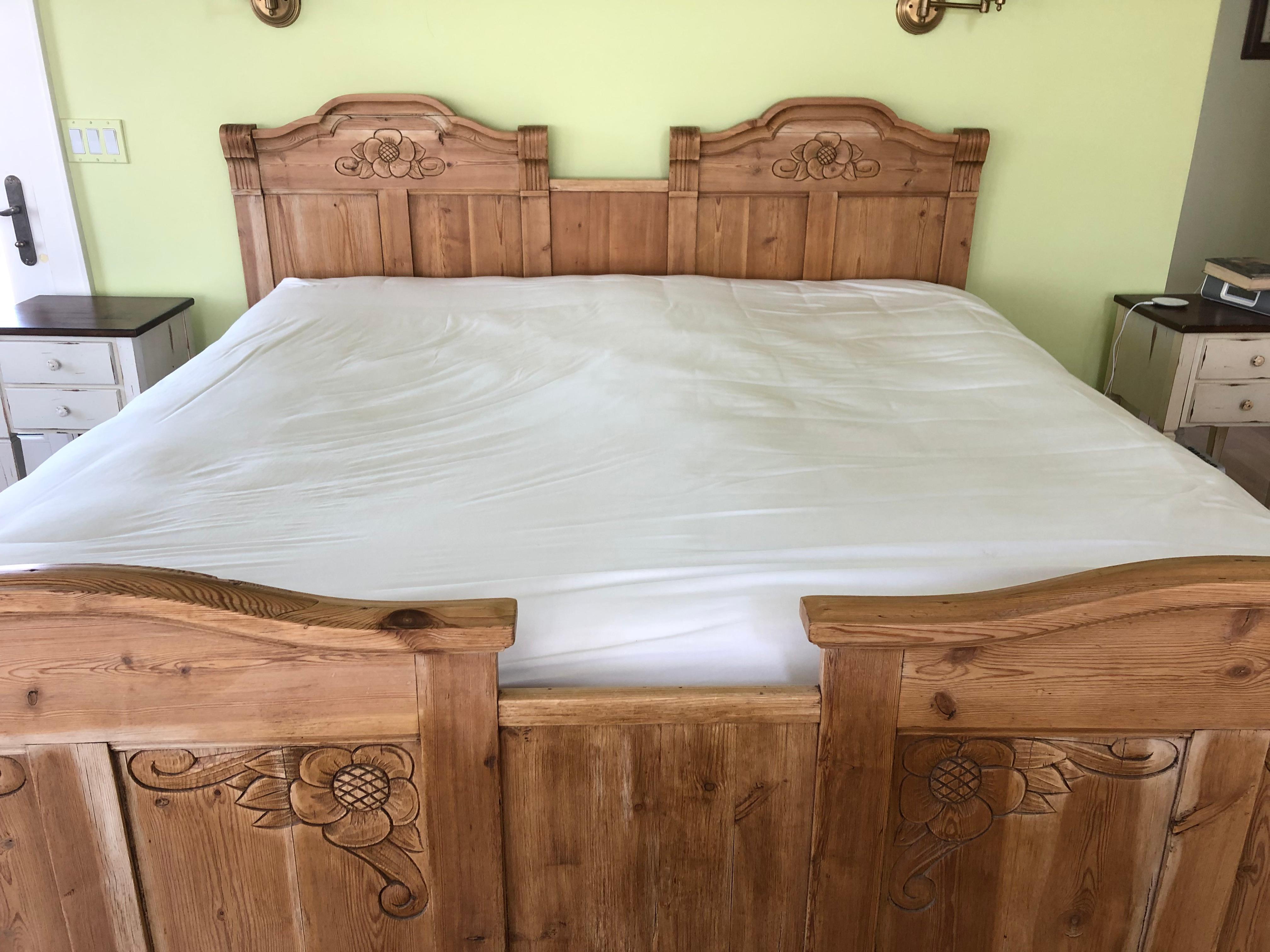 An impressive and charming antique natural pine king size bed having carved wood head and foot boards with folk art style flowers and matching side rails. Originally the bed was two twins, cleverly configured to make a king frame.
Footboard is