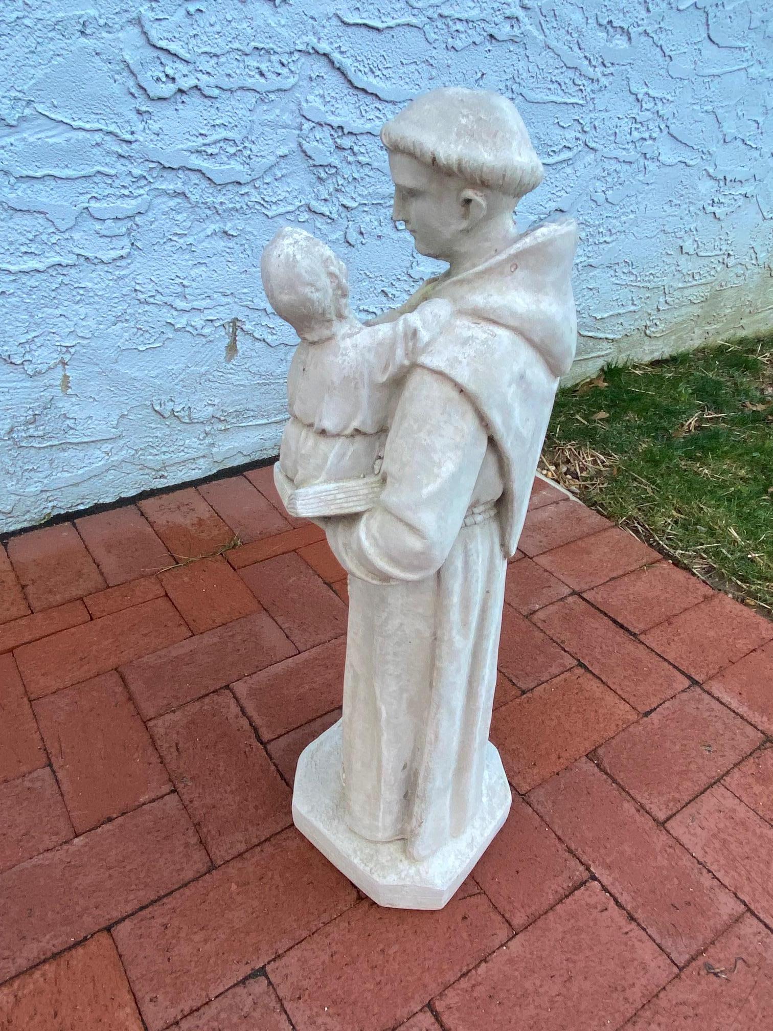 Lovely cement sculpture of St. Anthony draped in a monk's robe and holding a baby in his arms.