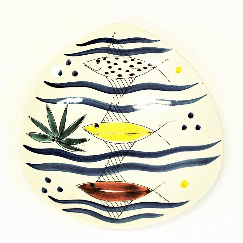 Coupe ou plat à fruits vintage en céramique modèle Omnia 76-140 conçu par Inger Waage par Stavangerflint, Norvège années 1950. Joli décor de poisson peint en émail avec des motifs marins aux couleurs vives sur un fond de couleur blanc cassé.
