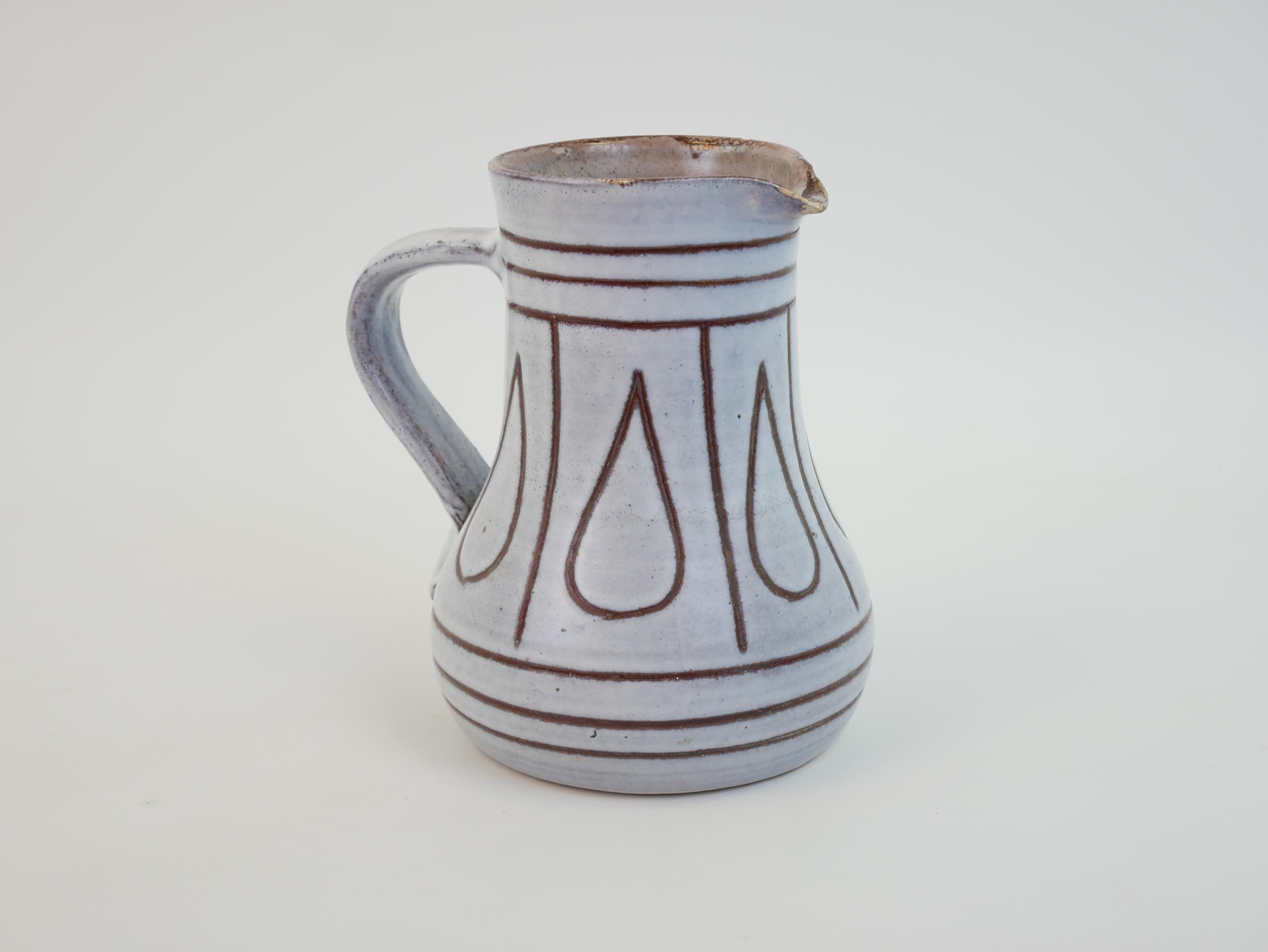 This charming ceramic pitcher, attributed to Jacques Innocenti, stands 14 cm tall with a 12 cm diameter. Its elegantly flared shape, reminiscent of traditional pottery, is enhanced by a delicately curved handle and a slightly irregular spout,