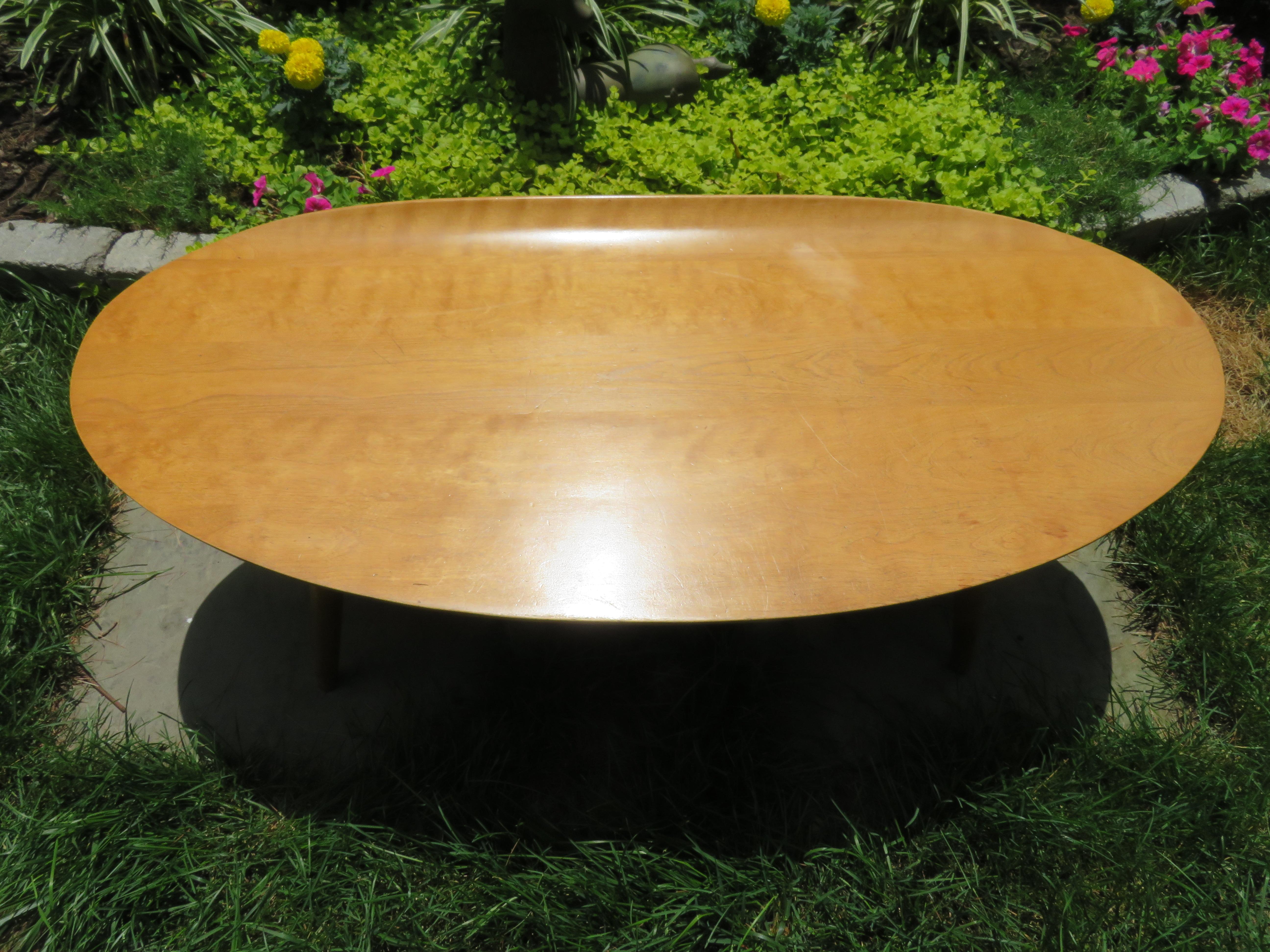 Lovely 1950s Russell Wright designed surfboard coffee or cocktail table with curved lip on one side. Beautiful warm toned maple surfboard shape sitting on 4 tapered turned legs. Russell Wright Conant ball markings are on underside of table. This