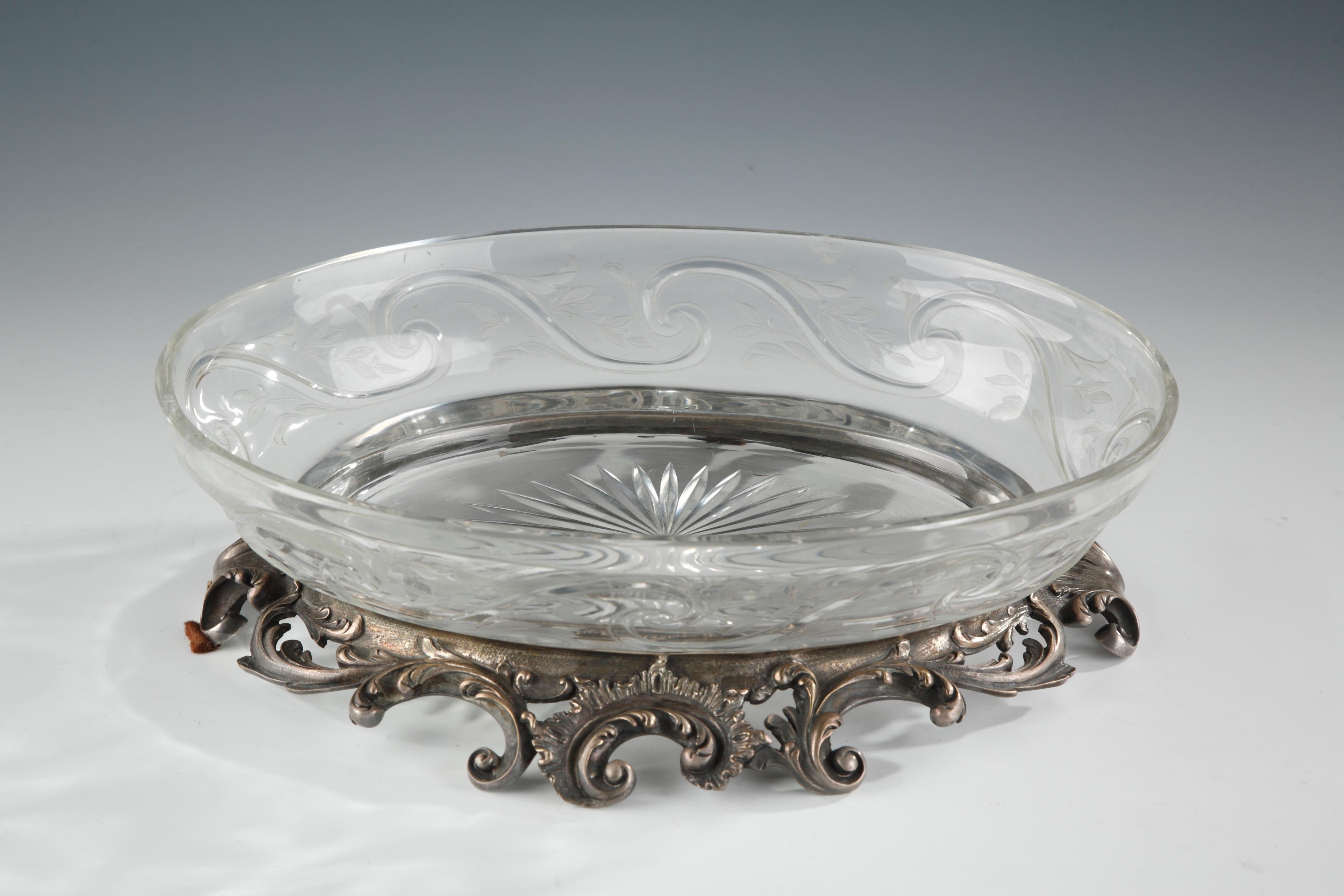 Signed Cardeilhac, Paris.

A jardinière consisting of an oval bowl in engraved crystal, decorated with a frieze of foliate waves and a rayed star in the bottom. It fits into a silver plated metal base ornamented with rococo motifs arranged